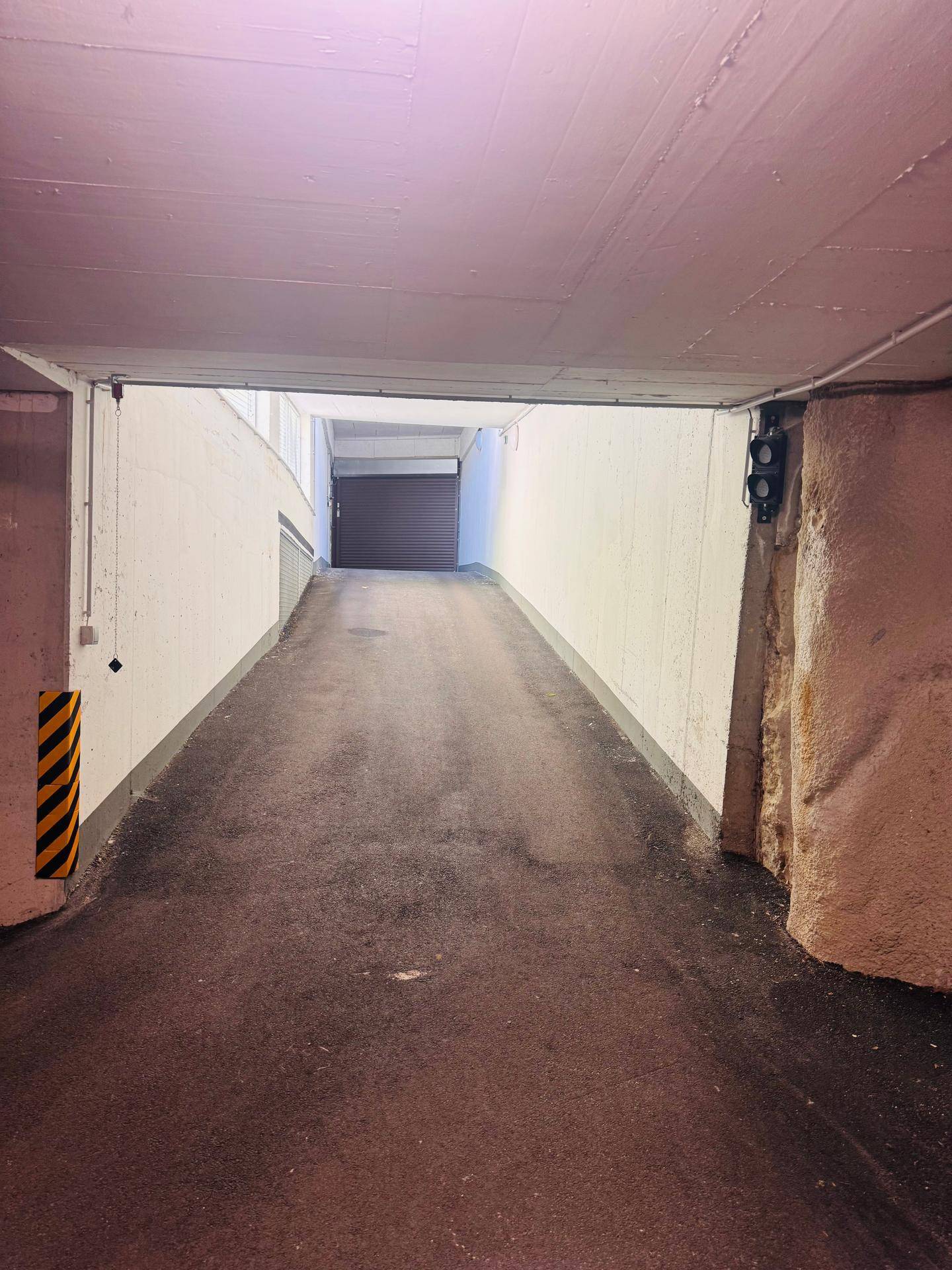 Zufahrtsrampe zu einer Tiefgarage mit Betonwänden und Beleuchtung.