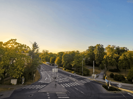 Luftaufnahme einer Straßenkreuzung mit Bäumen und Gebäuden bei Sonnenuntergang, ruhige Atmosphäre.