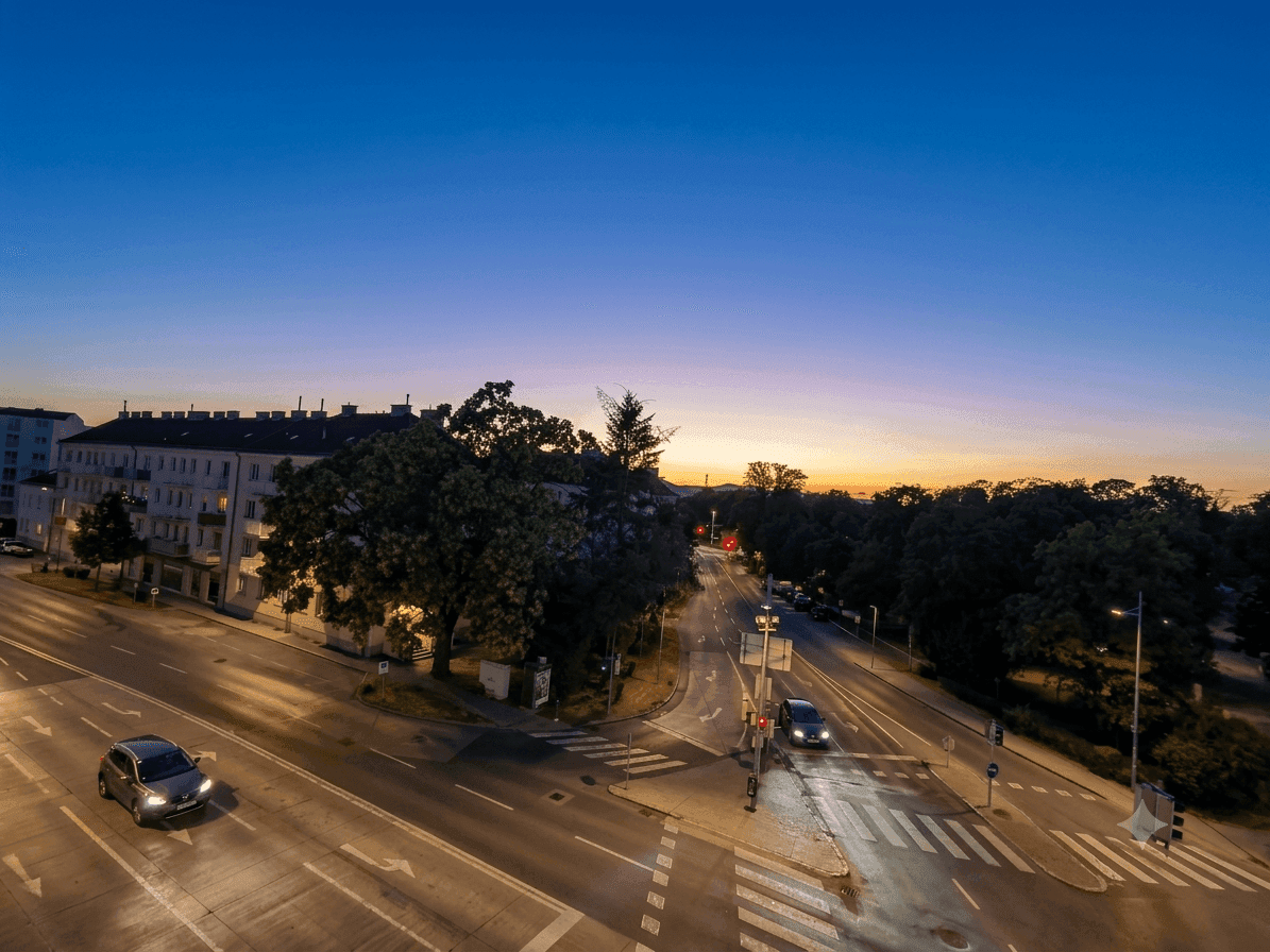 Abendliche Luftaufnahme einer belebten Straßenkreuzung mit Gebäuden und Bäumen in der Dämmerung.