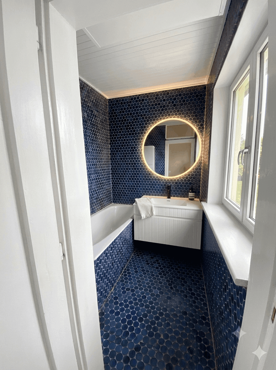 Modernes Badezimmer mit blauen Mosaikfliesen, Badewanne und beleuchtetem Spiegel, sehr stilvoll.
