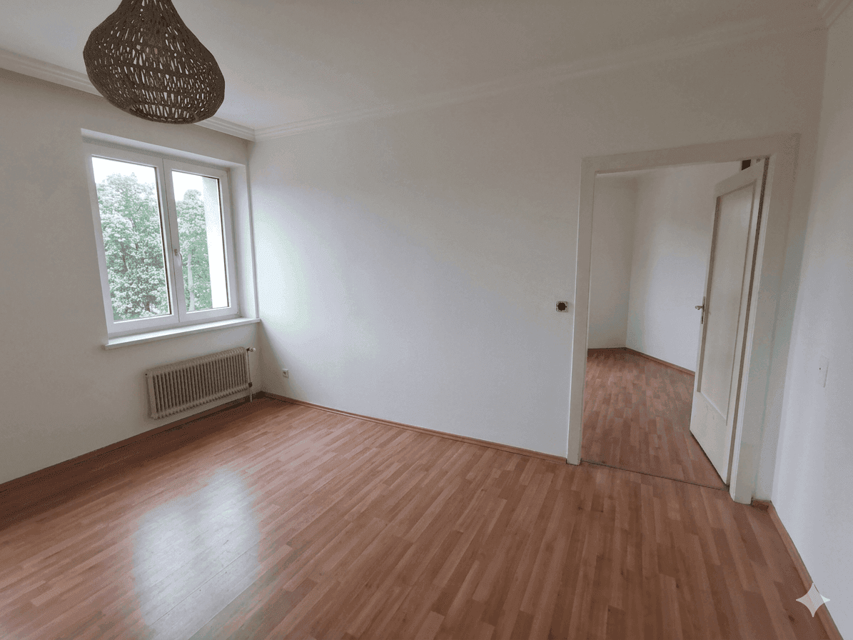 Geräumiges, leeres Wohnzimmer mit Holzboden und großen Fenstern, bereit zur individuellen Gestaltung.