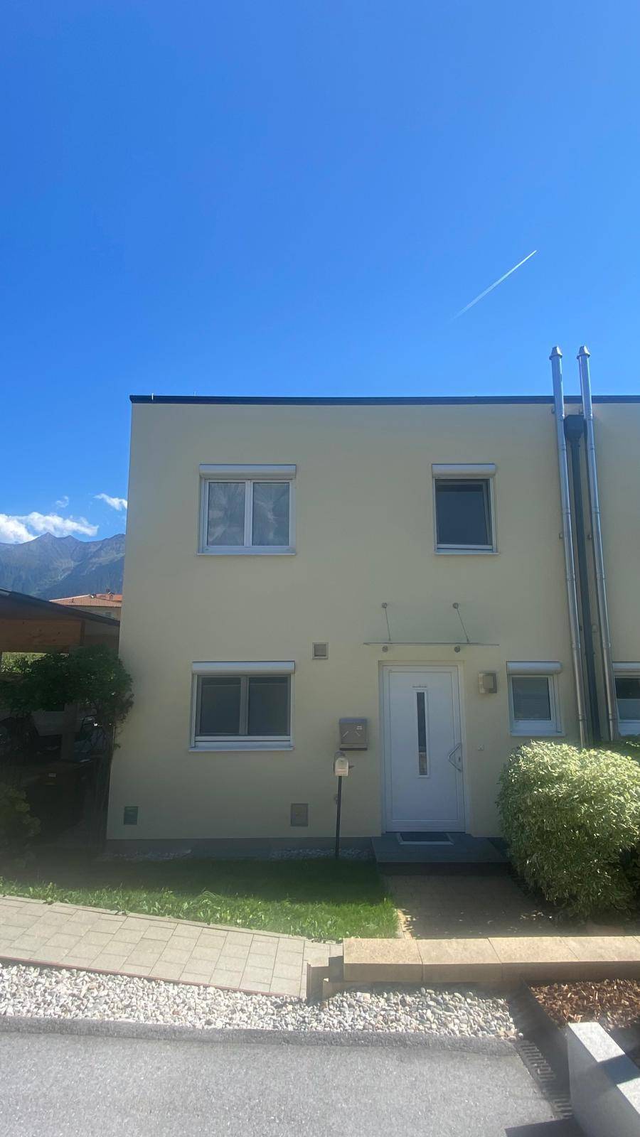Frontansicht des modernen Reihenhauses mit heller Fassade, Eingangstür und Fenstern mit Rollläden.