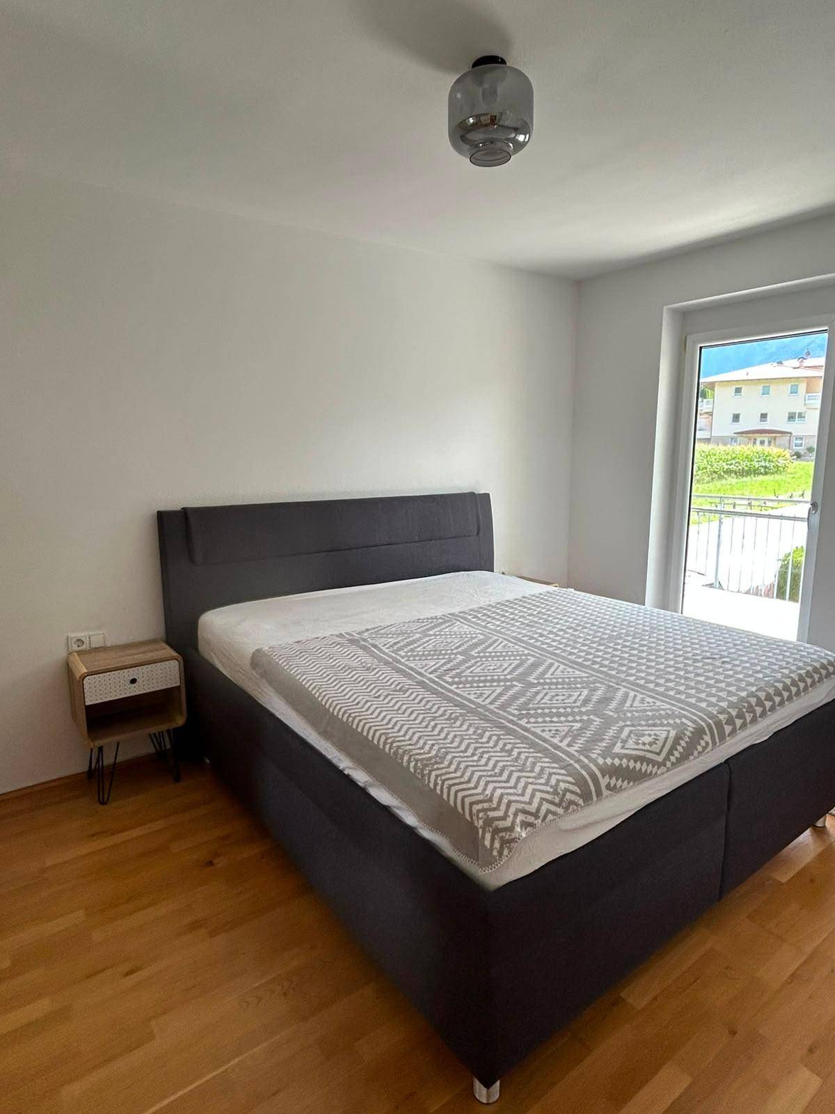 Schlafzimmer mit Doppelbett, Holzboden und Zugang zu einem Balkon.