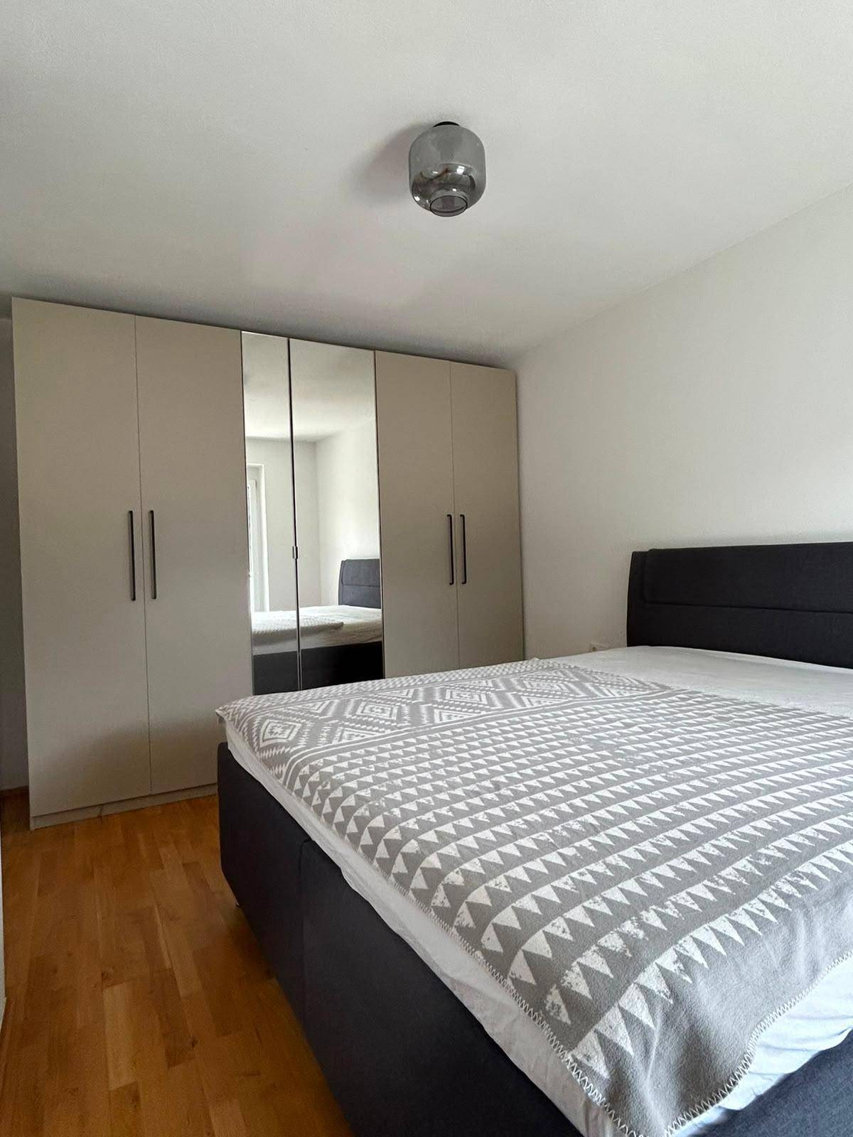 Schlafzimmer mit Doppelbett, großem Spiegelschrank und Holzboden.