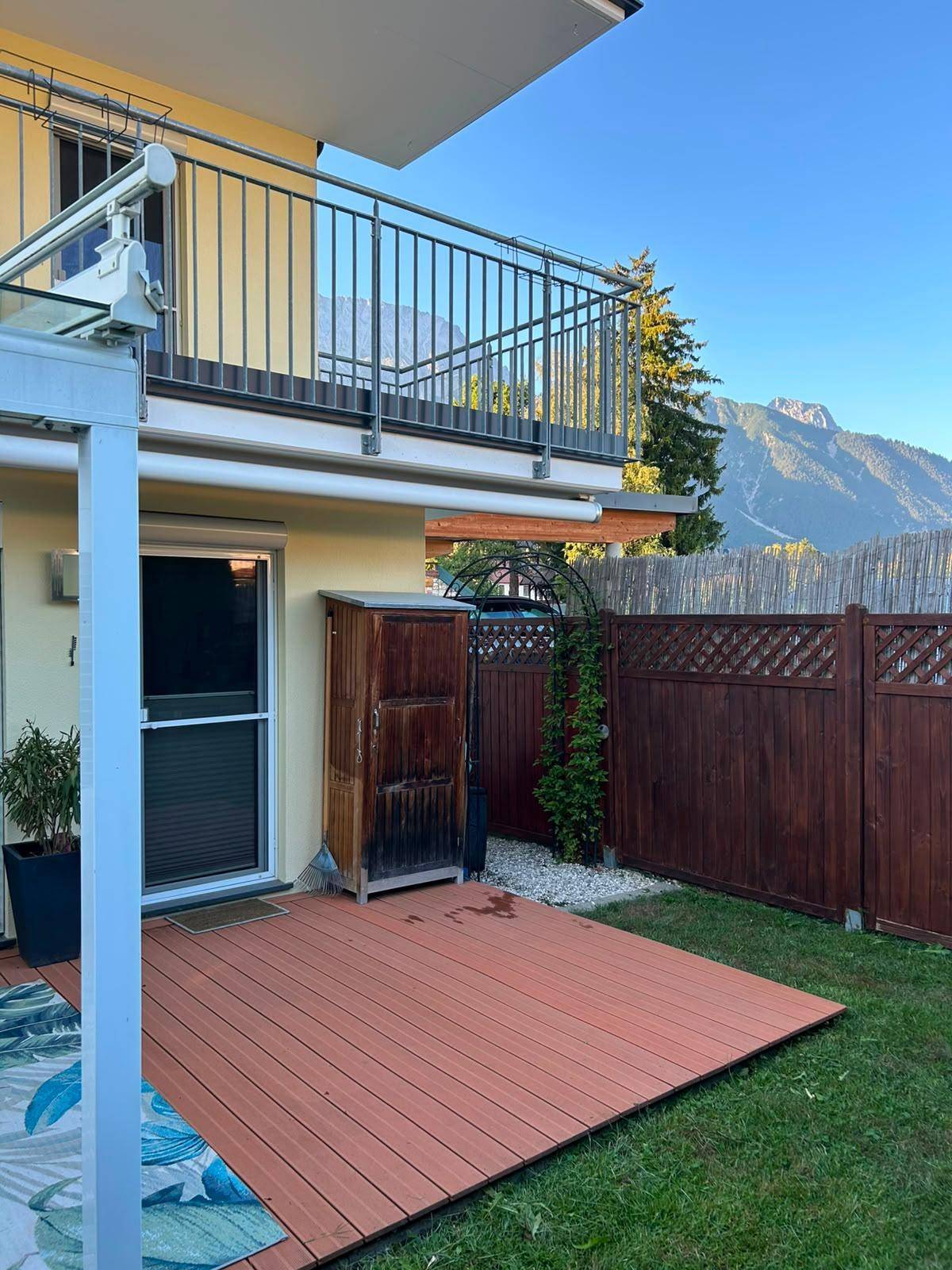 Terrasse mit Holzdeck und Zugang zum Garten, im Hintergrund die beeindruckende Berglandschaft.