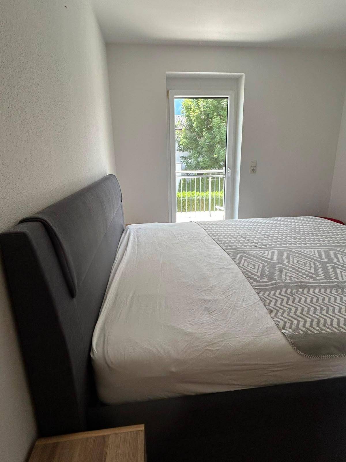Schlafzimmer mit Doppelbett und Zugang zu einem Balkon mit Blick ins Grüne.