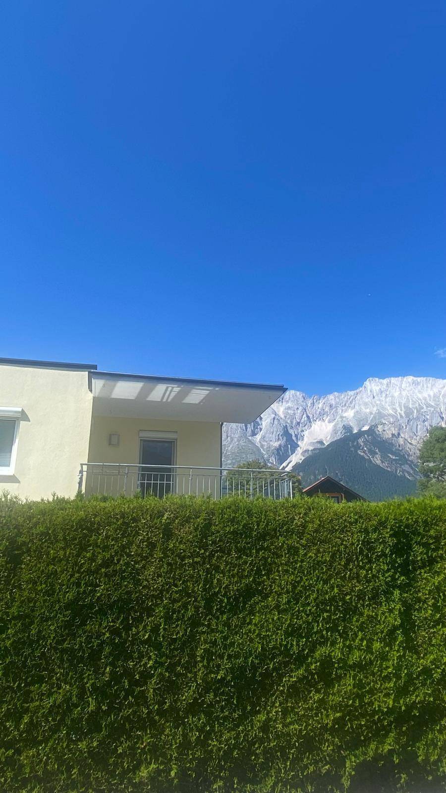 Balkon mit Blick auf die majestätischen Berge und eine hohe Hecke, die Privatsphäre bietet.
