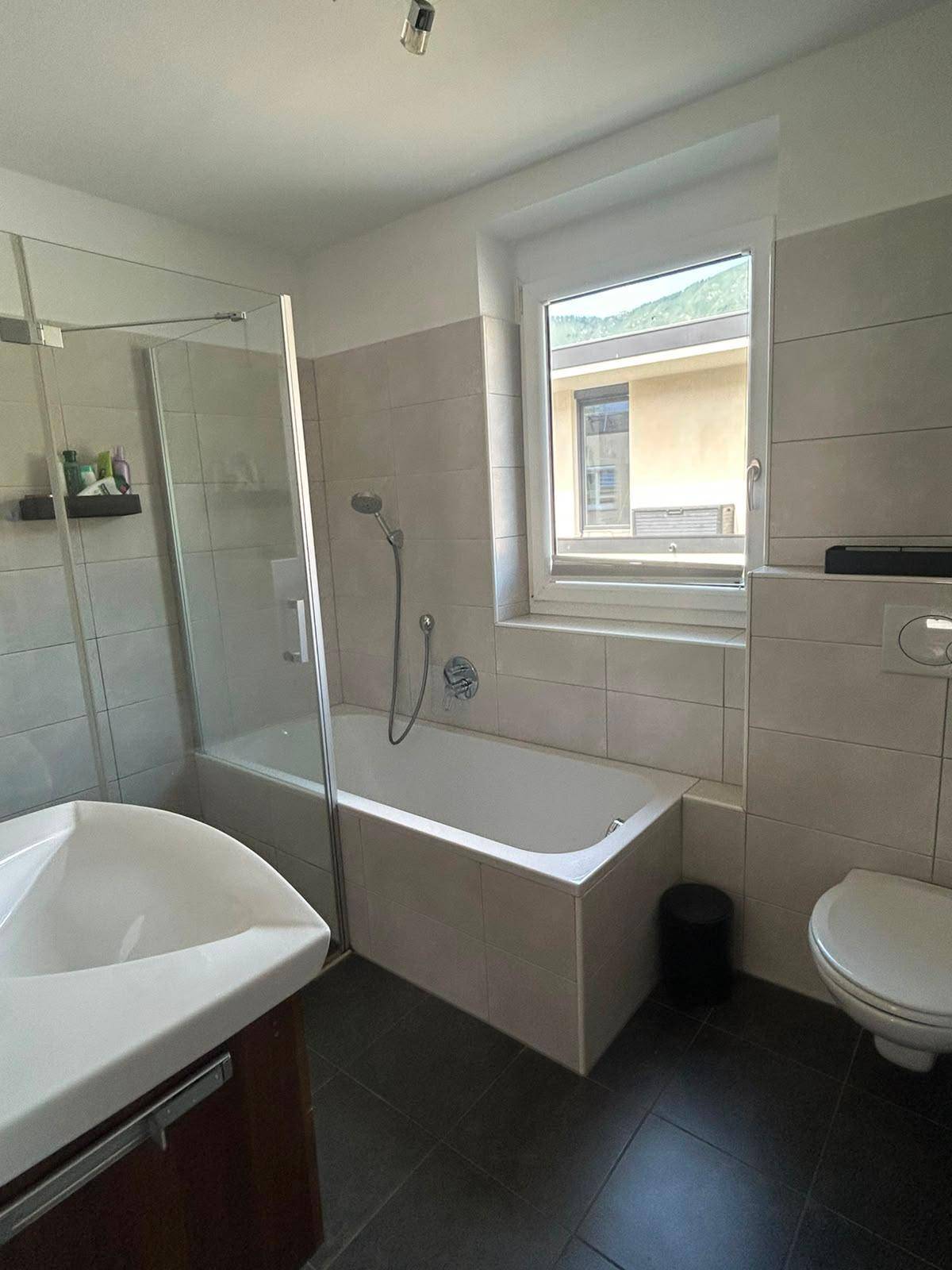 Helles Badezimmer mit Badewanne, integrierter Dusche und Fenster mit Bergblick.
