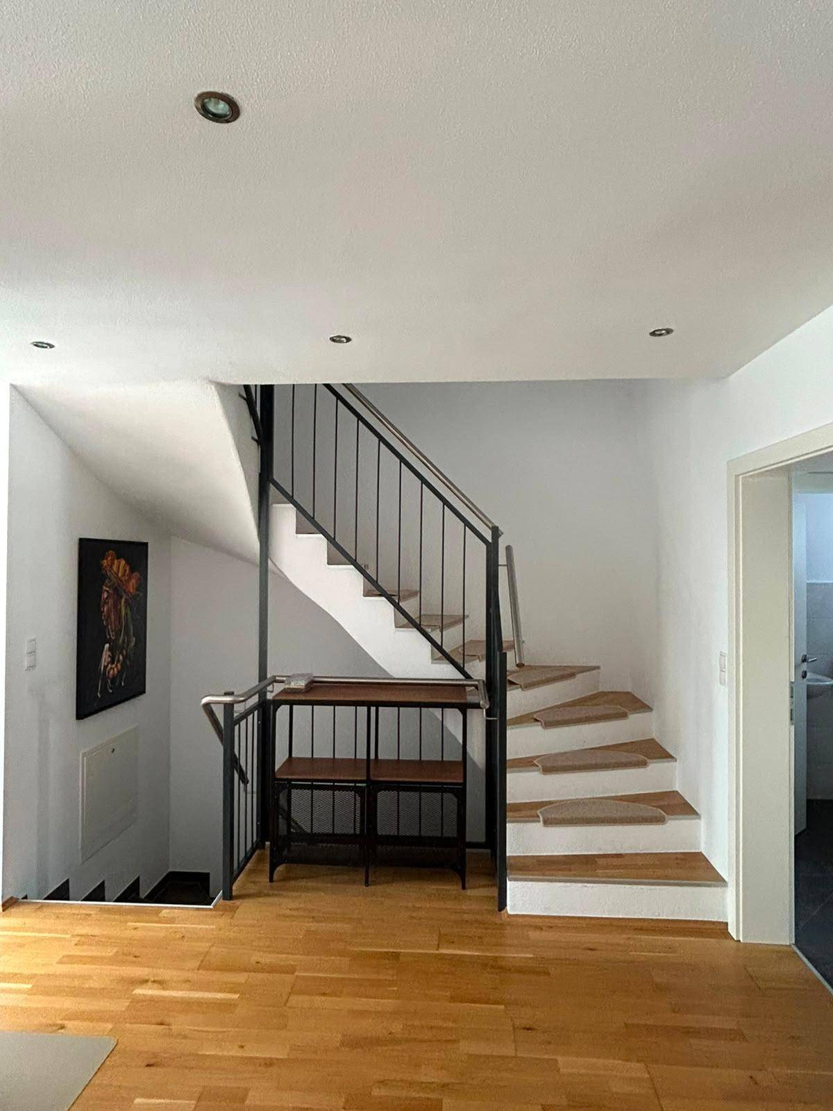 Geräumiger Flur mit Holztreppe und minimalistischer Einrichtung, die Helligkeit betont.