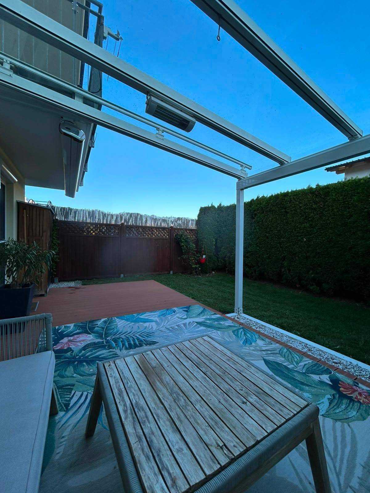 Terrasse mit Holzdeck und Gartenmöbeln unter einer Glasüberdachung, ideal für entspannte Abende.