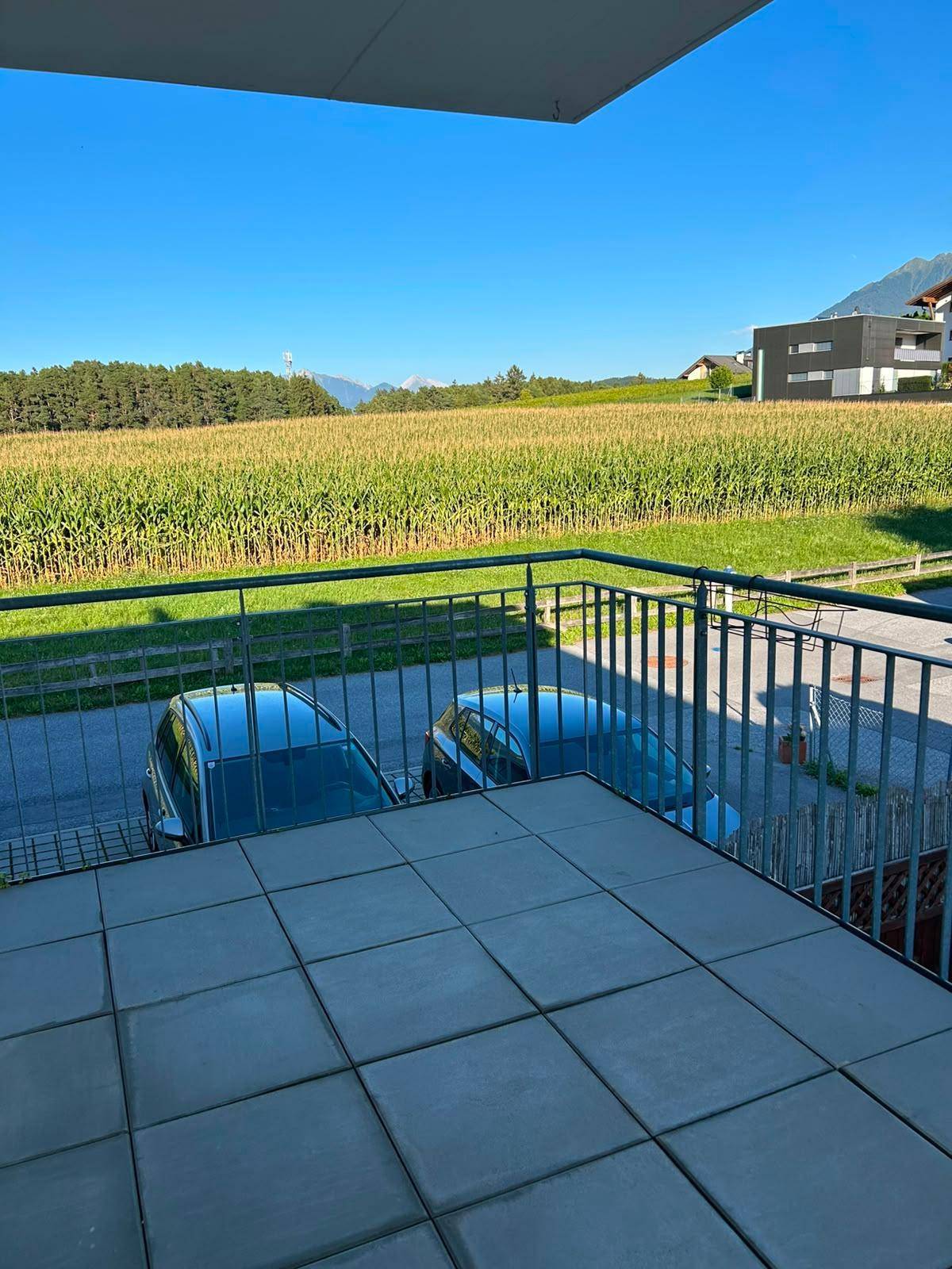 Blick vom Balkon auf ein weites Maisfeld und die umliegende Landschaft unter blauem Himmel.