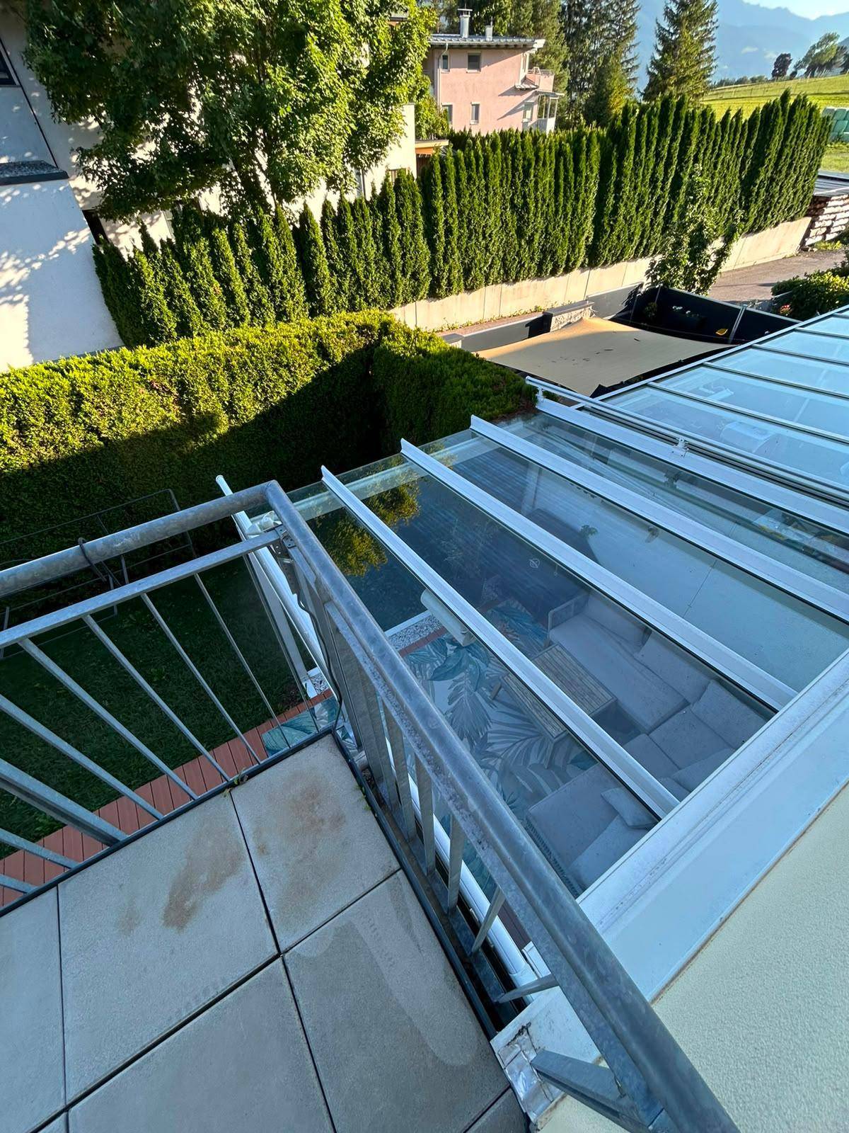 Blick vom Balkon hinunter auf die überdachte Terrasse und den grünen Gartenbereich des Hauses.