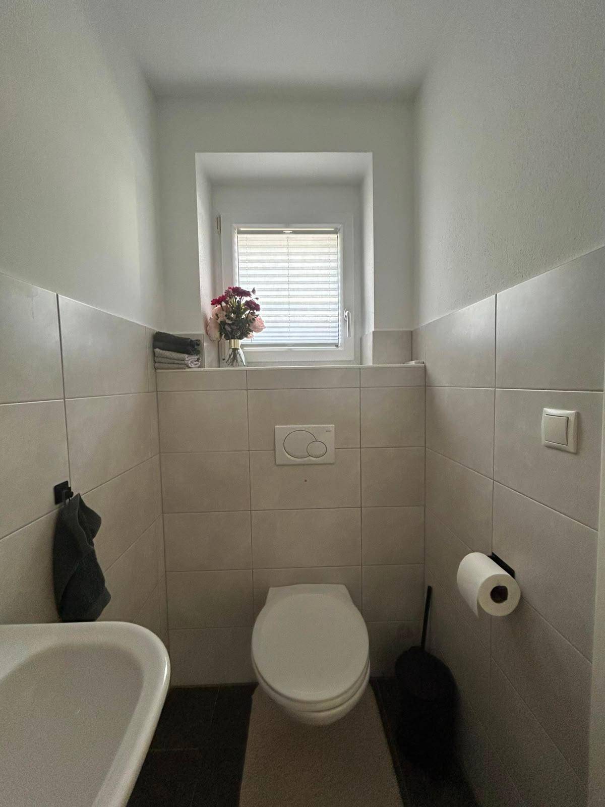 Modernes Gäste-WC mit Fenster, Wand-WC und dunklen Bodenfliesen.