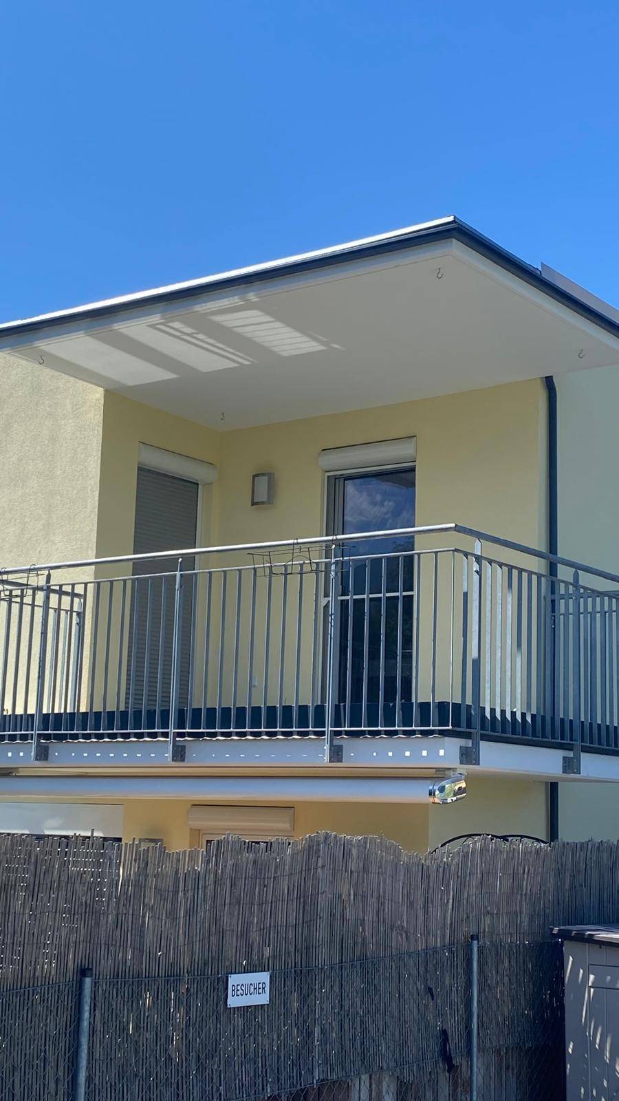 Detailansicht des Balkons mit Metallgeländer und Rollläden an den Fenstern der oberen Etage.