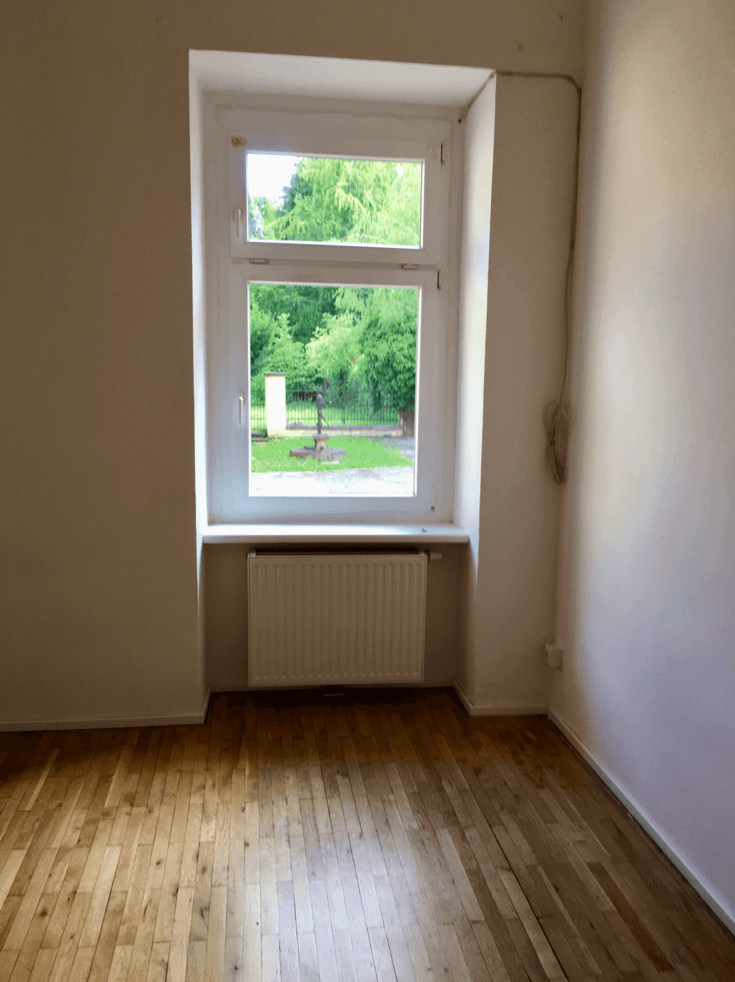 Heller Raum mit großem Fenster, Holzfußboden und Blick ins Grüne.