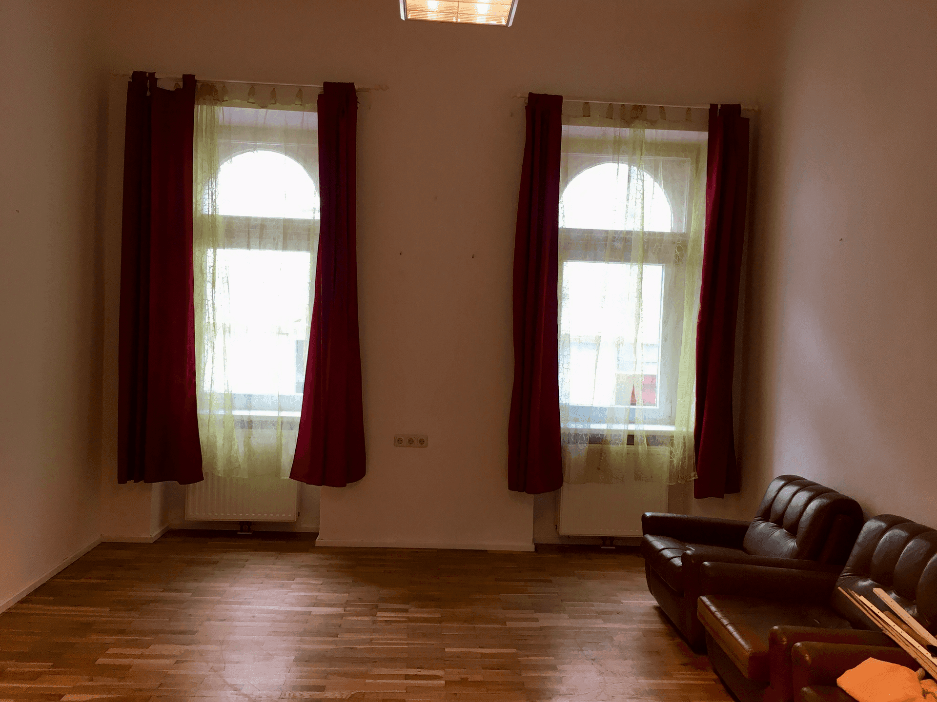 Wohnzimmer mit zwei hohen Rundbogenfenstern, Holzfußboden und Ledersofa.