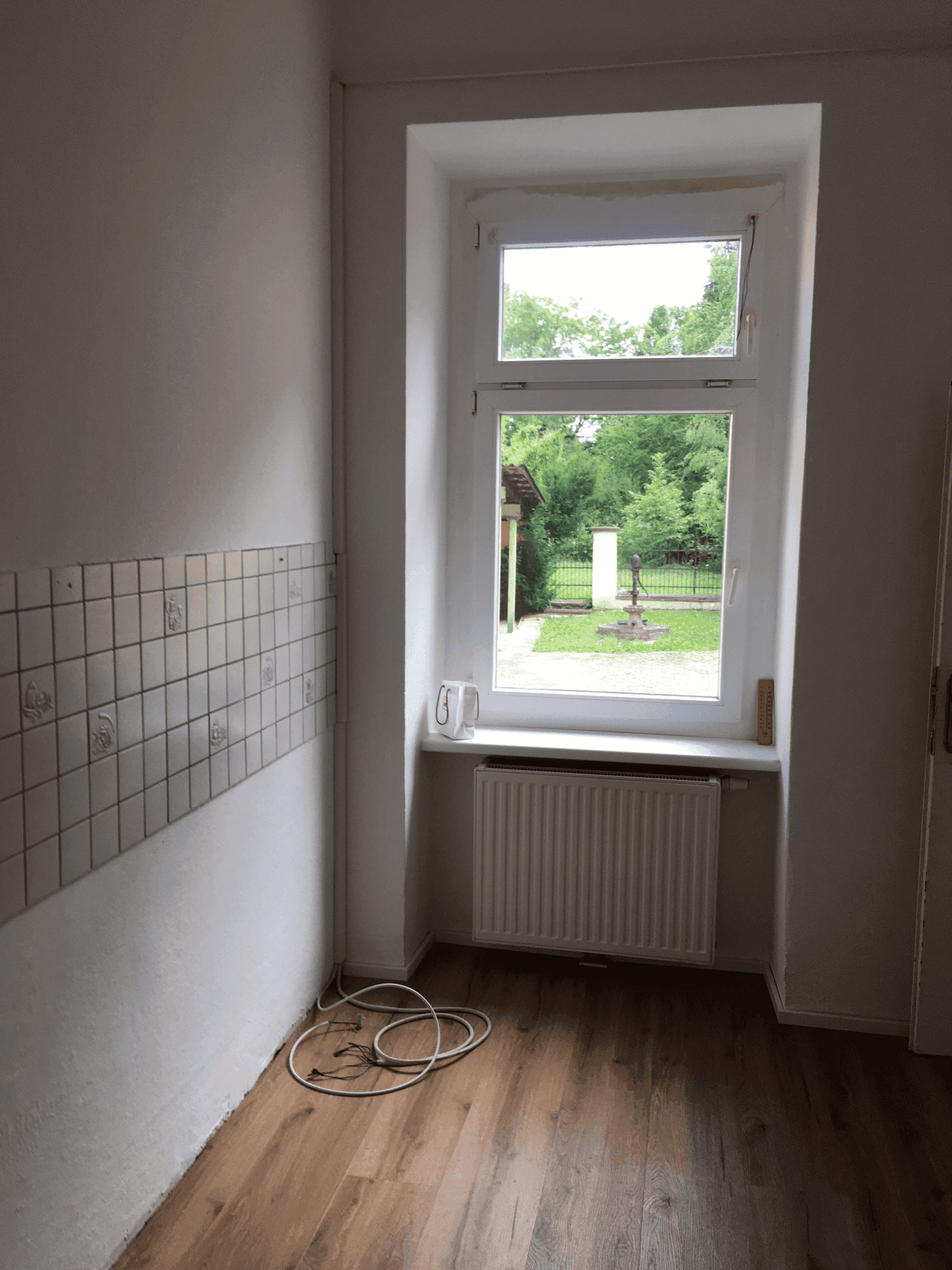 Kleine Küche mit Fenster, Fliesenwand und Blick ins Grüne.