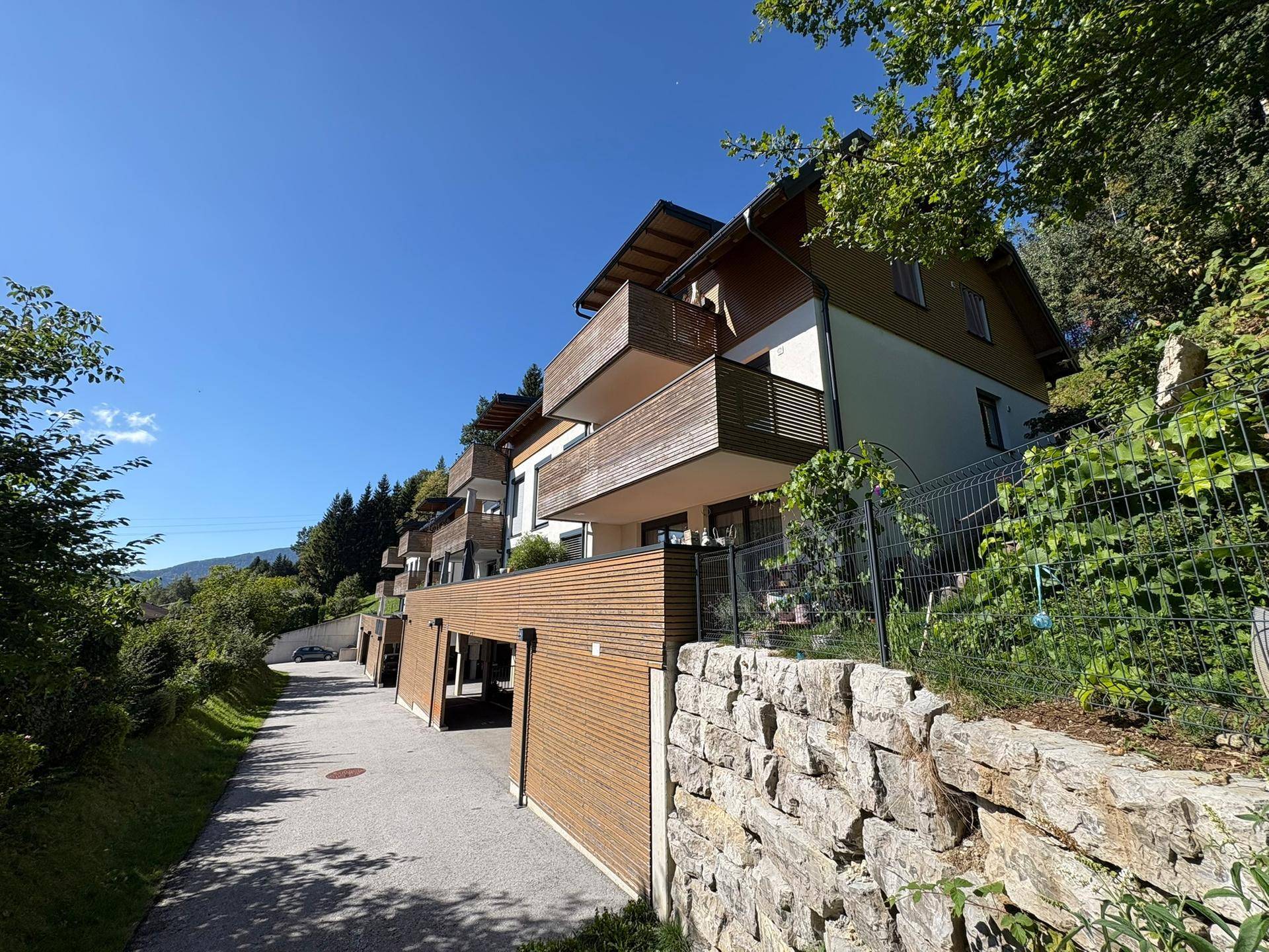 Moderne Wohnanlage mit Holzfassade, Balkonen und Zufahrt in grüner Hanglage.