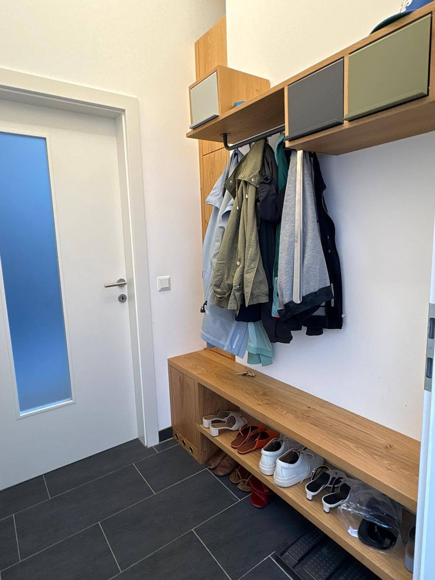 Eingangsbereich mit Garderobe, Schuhablage und dunklen Fliesen, praktisch und funktional gestaltet.
