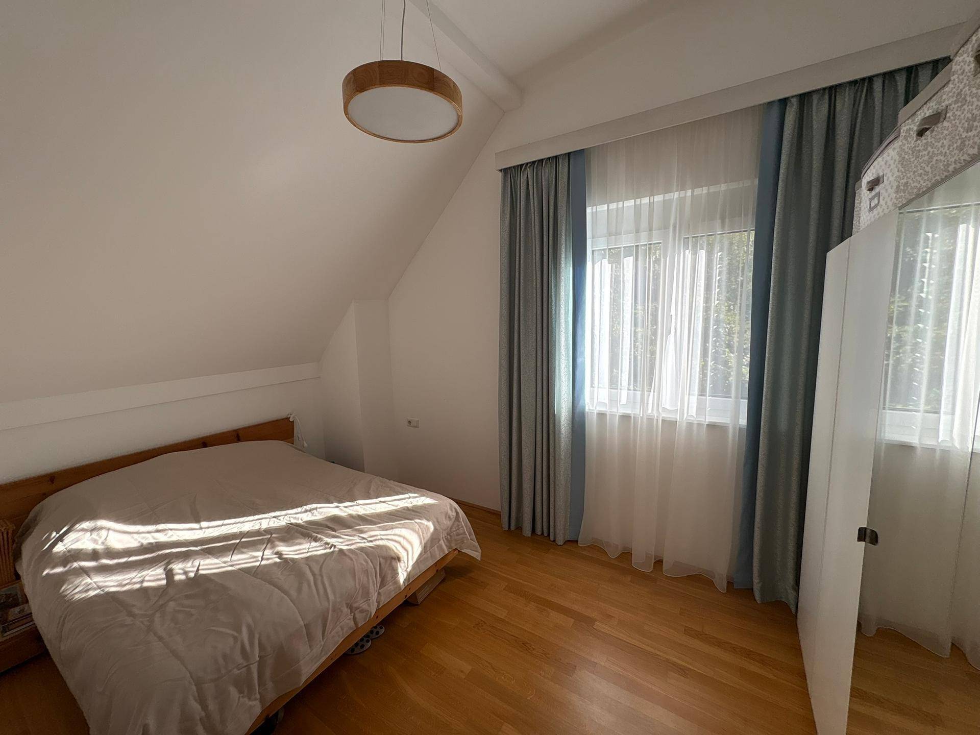 Gemütliches Schlafzimmer mit Holzbett, Parkettboden und Fenster mit Vorhängen unter einer Dachschräge.