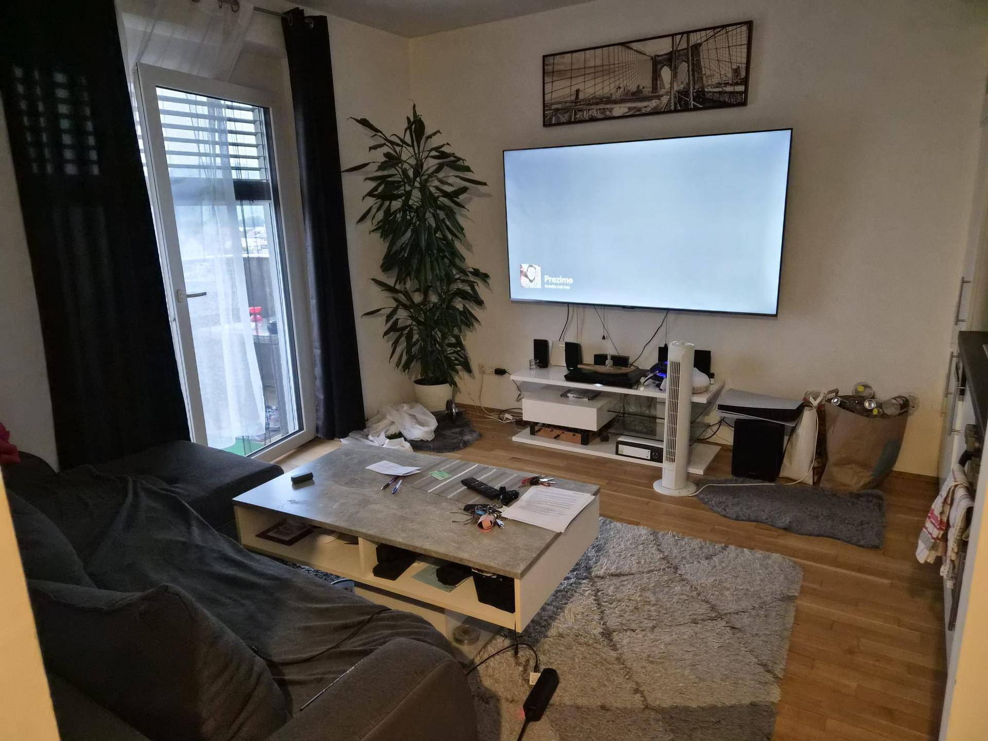 Wohnzimmer mit großem Fernseher, Sofa, Couchtisch und Zugang zum Balkon.