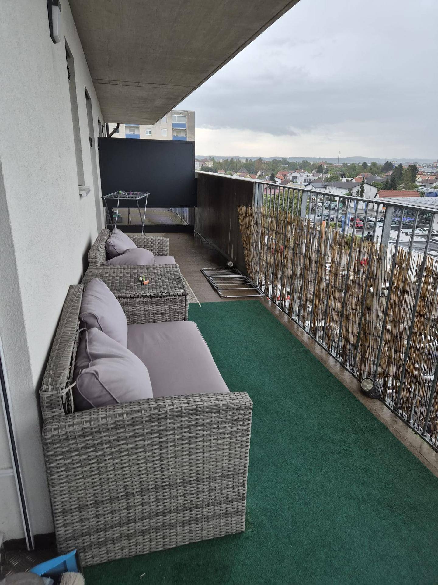 Möblierter Balkon mit Rattanmöbeln, Kunstrasen und Blick auf die Stadt.