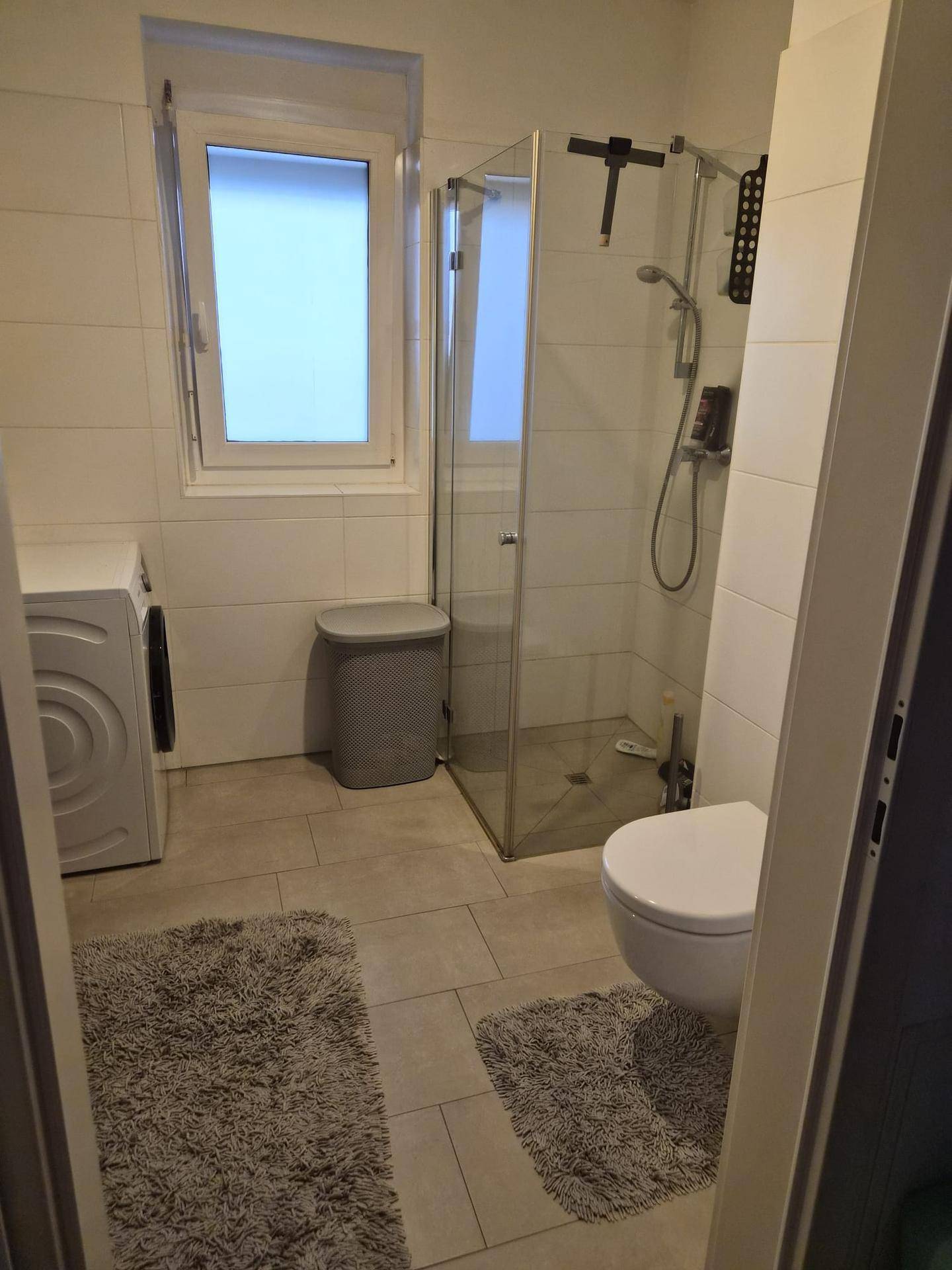 Modernes Badezimmer mit Dusche, WC, Waschmaschine und Fenster für Tageslicht.