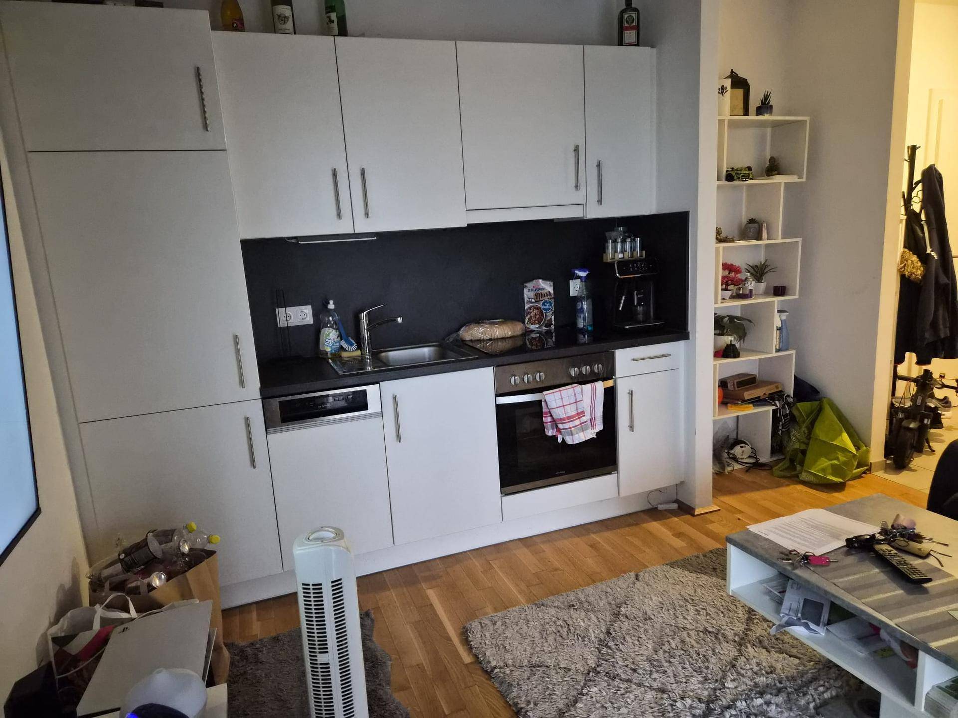 Moderne Küchenzeile mit weißen Schränken, schwarzer Arbeitsplatte und integriertem Backofen.