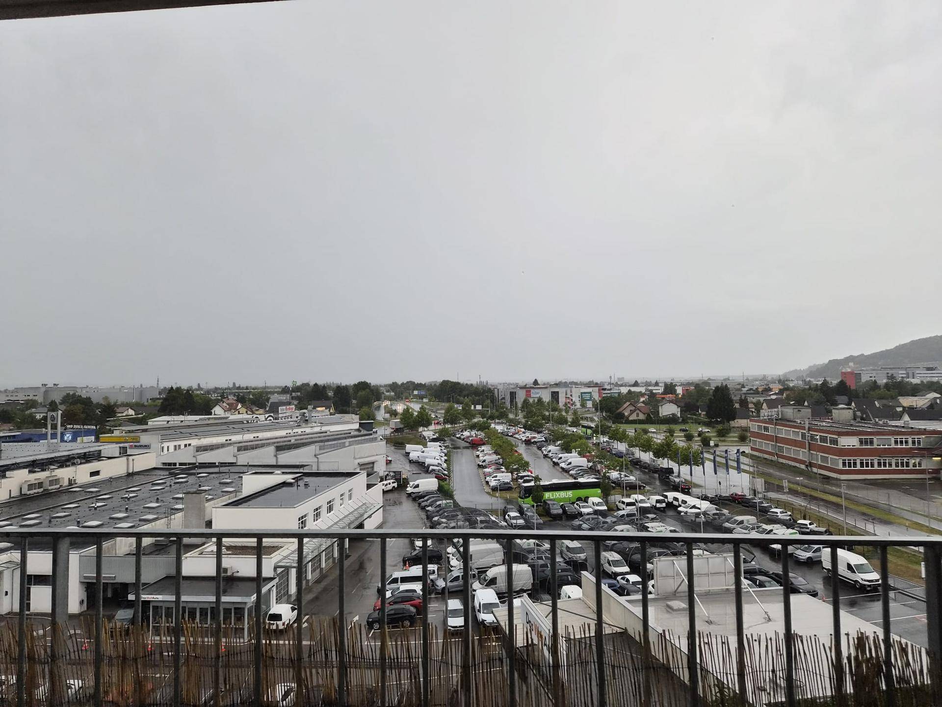 Weitläufiger Blick von einem Balkon über eine städtische Landschaft mit Parkplätzen und Gebäuden.