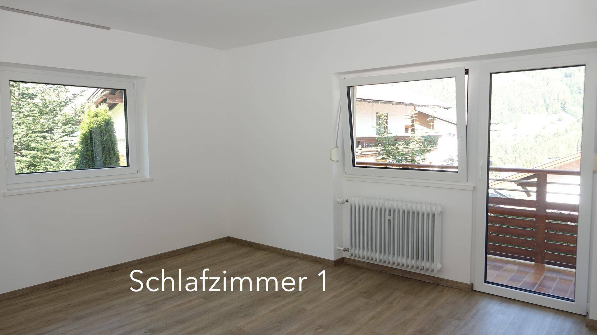 Helles Schlafzimmer mit Laminatboden, weißen Wänden und Zugang zu einem Balkon.