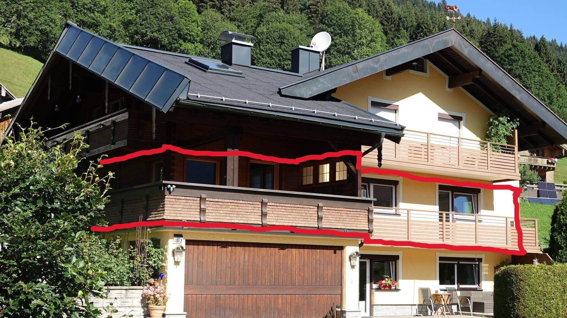 Ansicht eines traditionellen Hauses mit Holzbalkonen und Satteldach, umgeben von grüner Landschaft.
