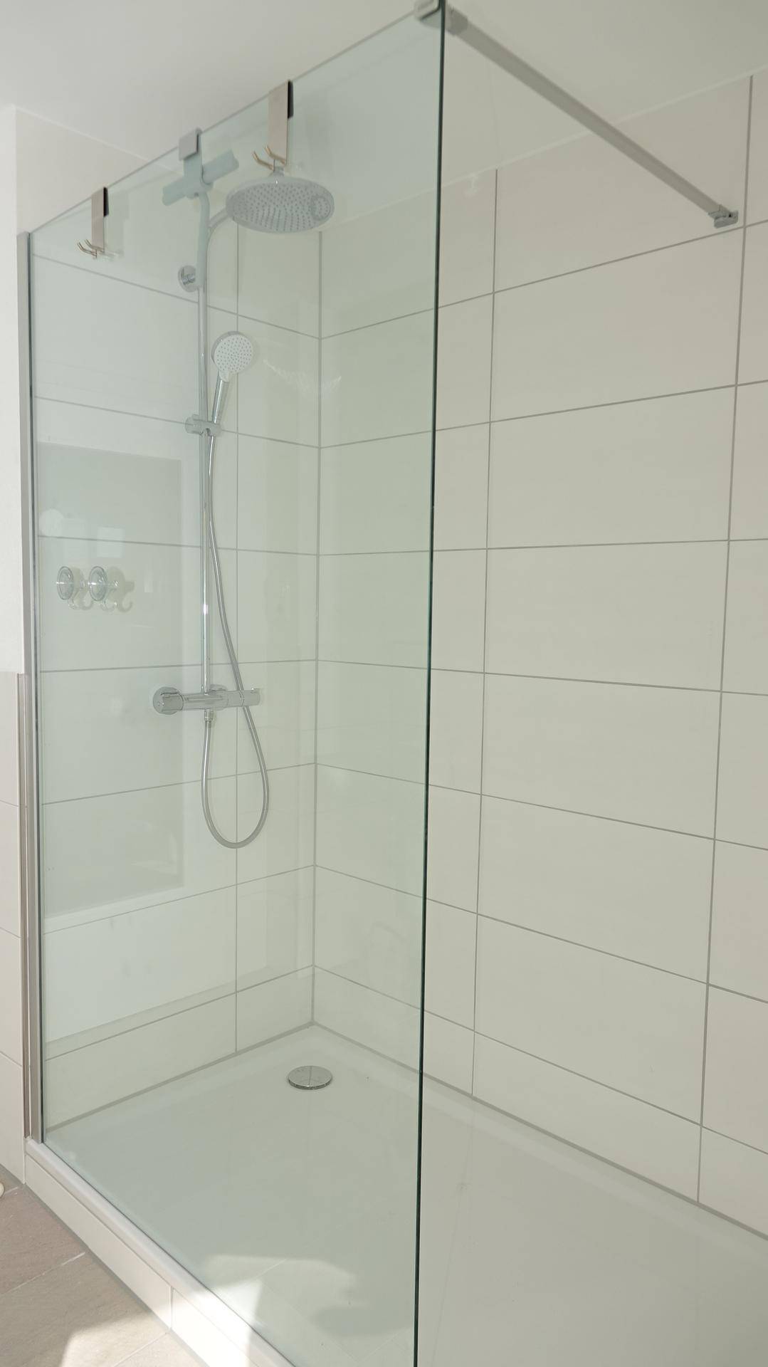 Geräumige, moderne Duschkabine mit Glasabtrennung und weißen Fliesen, ausgestattet mit einer Regendusche.