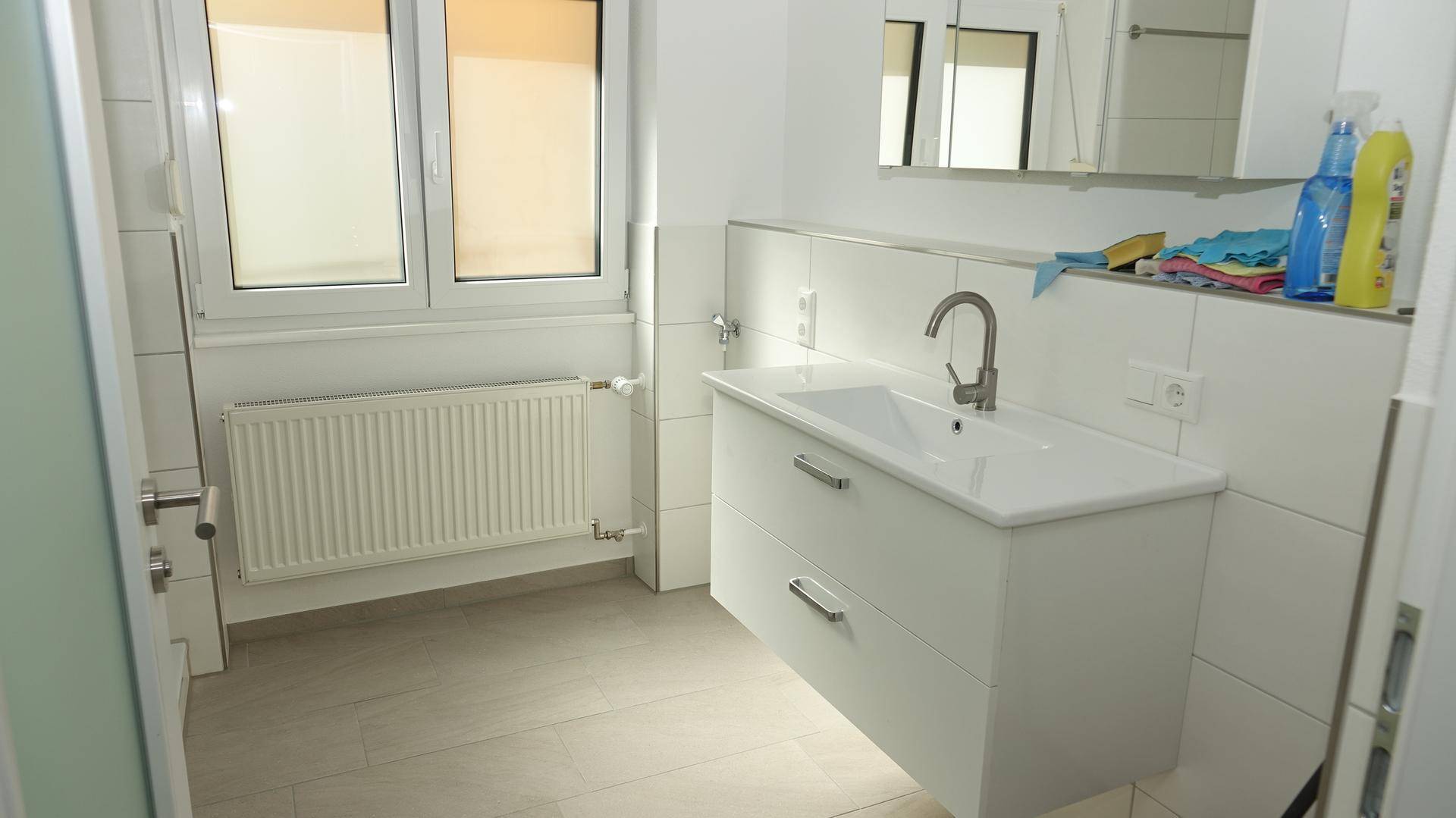 Helles Badezimmer mit Waschtisch, Spiegelschrank, Fenster und Heizkörper, in modernem Design.