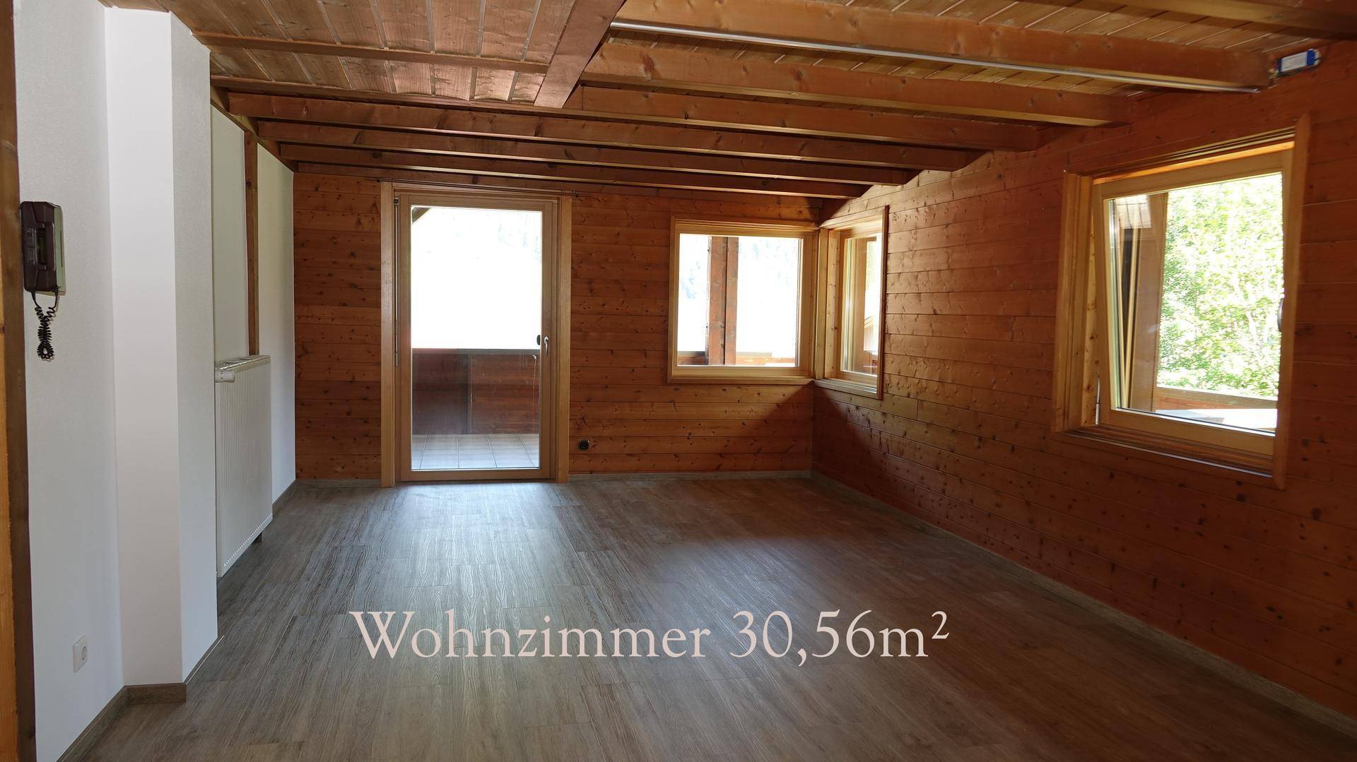 Gemütliches Wohnzimmer mit Holzwänden und -decke, Laminatboden und Zugang zu einem Außenbereich.
