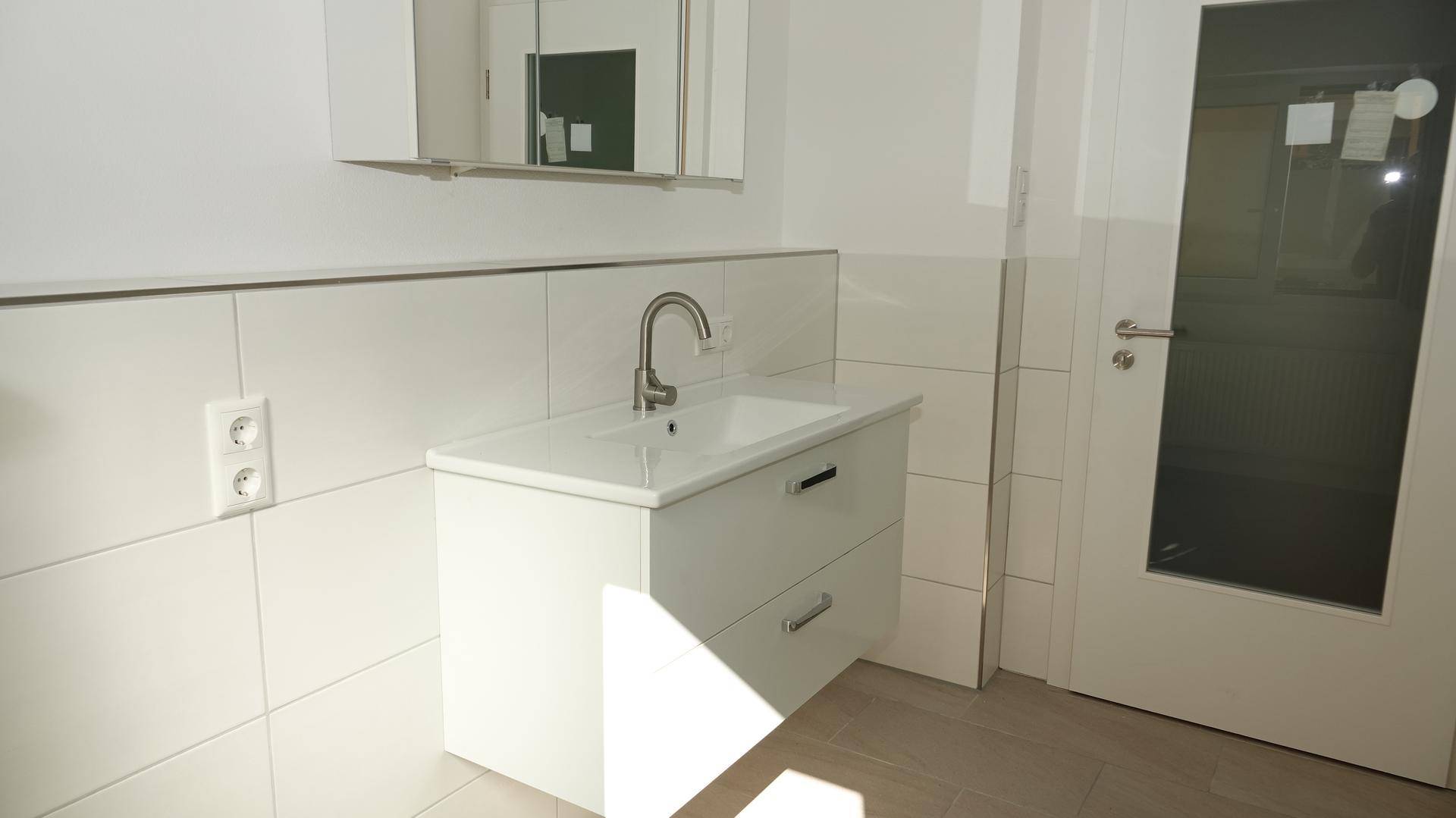 Modernes Badezimmer mit weißem Waschtischunterschrank, Einzelwaschbecken und Spiegelschrank.