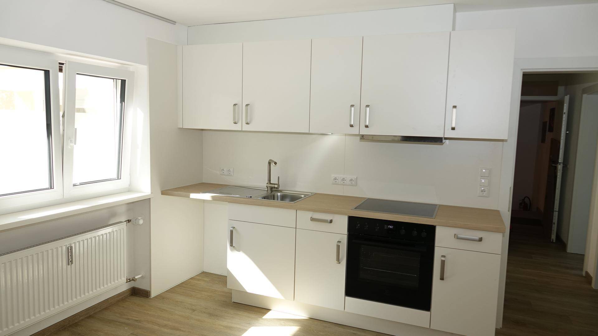 Helle, moderne Küche mit weißen Schränken, Holzarbeitsplatte und Fenster für natürliches Licht.