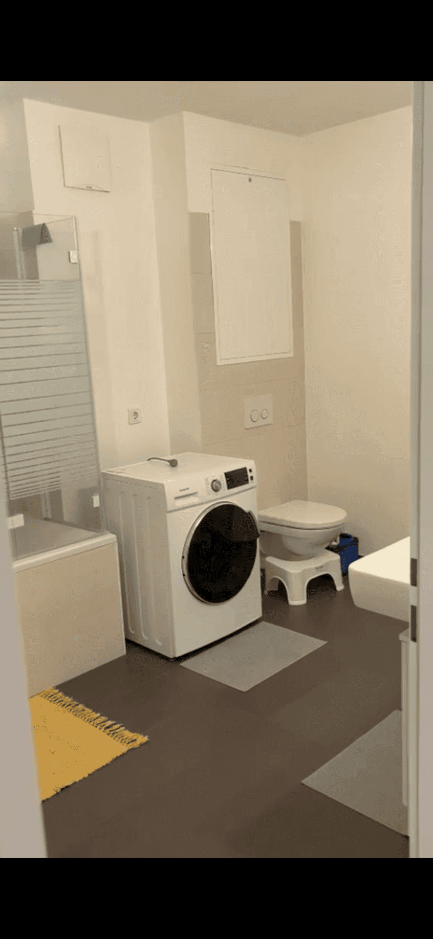 Badezimmer mit Toilette, Waschmaschine und Dusch-Badewannen-Kombination.