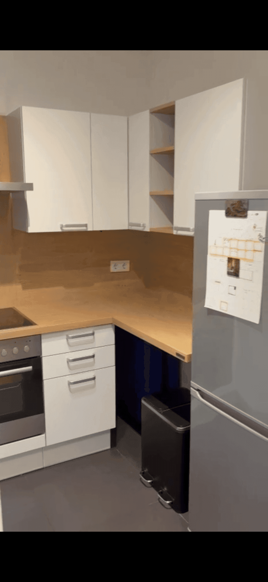 Funktionale Küche mit Kühlschrank, weißen Oberschränken und Holz-Arbeitsplatte.