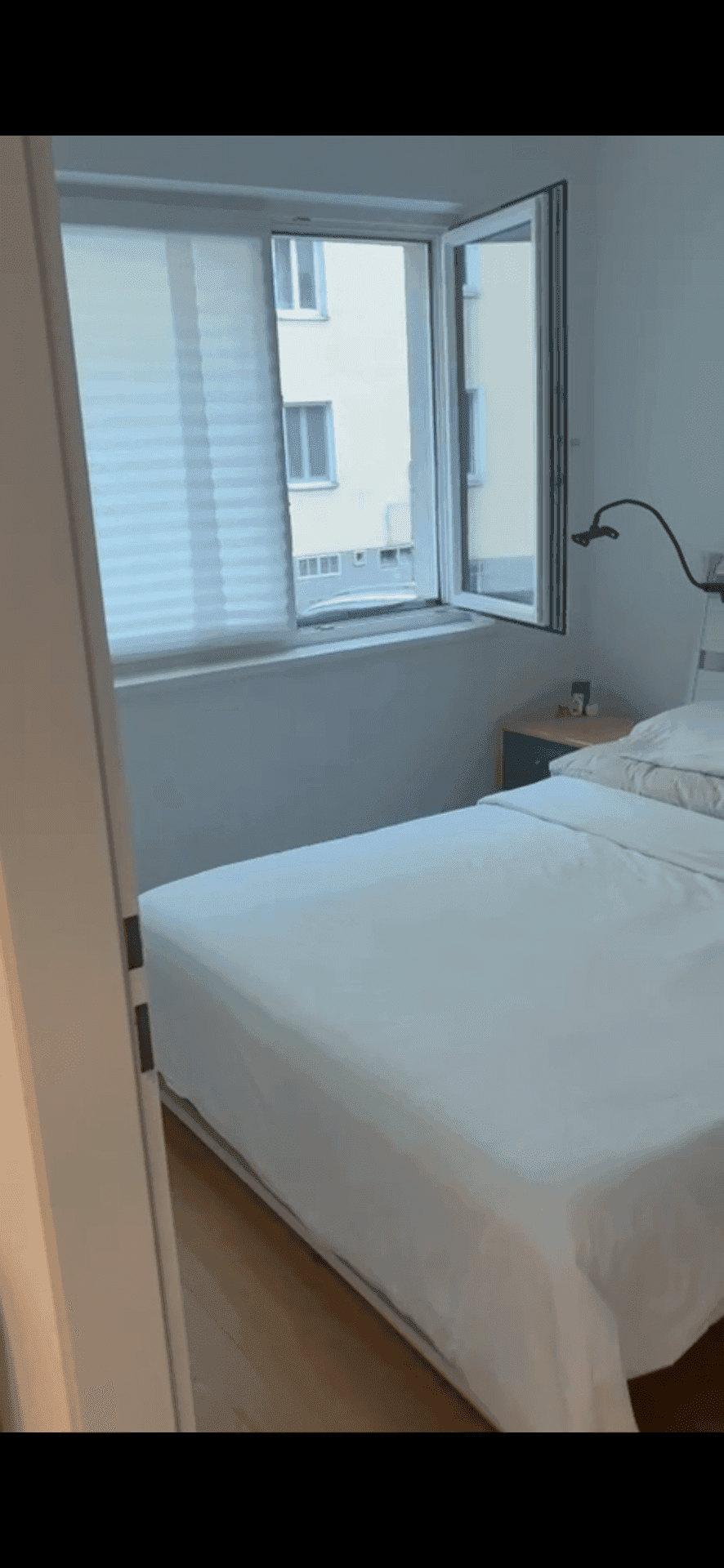 Schlafzimmer mit Einzelbett, Nachttisch und geöffnetem Fenster für frische Luft.