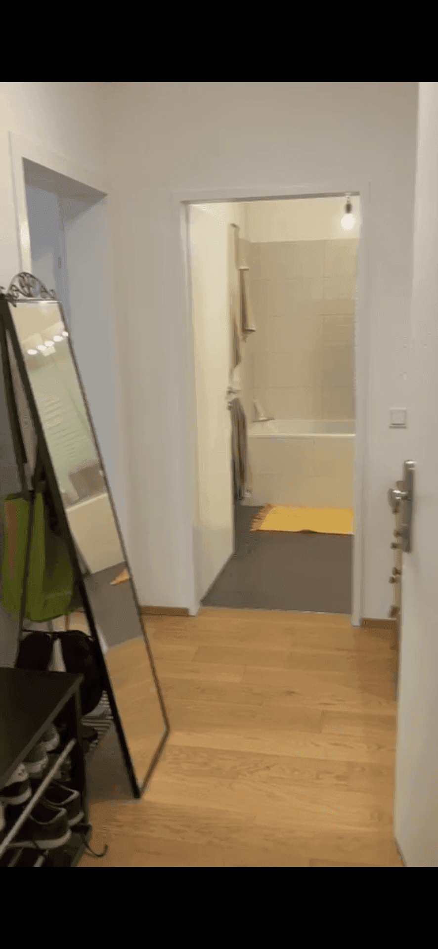 Heller Flur mit großem Spiegel und Blick in das Badezimmer mit Badewanne.