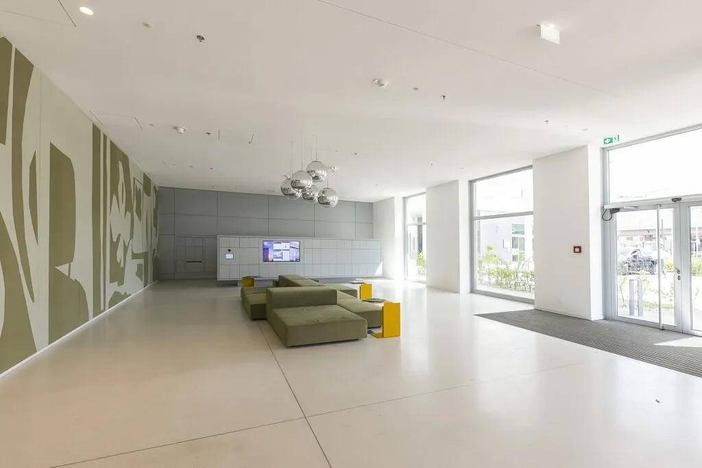 Geräumige, moderne Lobby mit minimalistischem Design, grünen Sitzgelegenheiten und großen Fenstern.