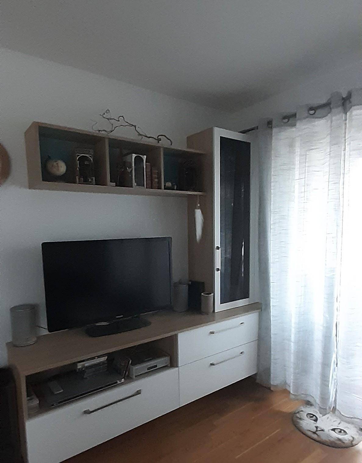 Heller Wohnbereich mit TV-Möbel und einem großen Fenster, das viel Tageslicht in den Raum lässt.