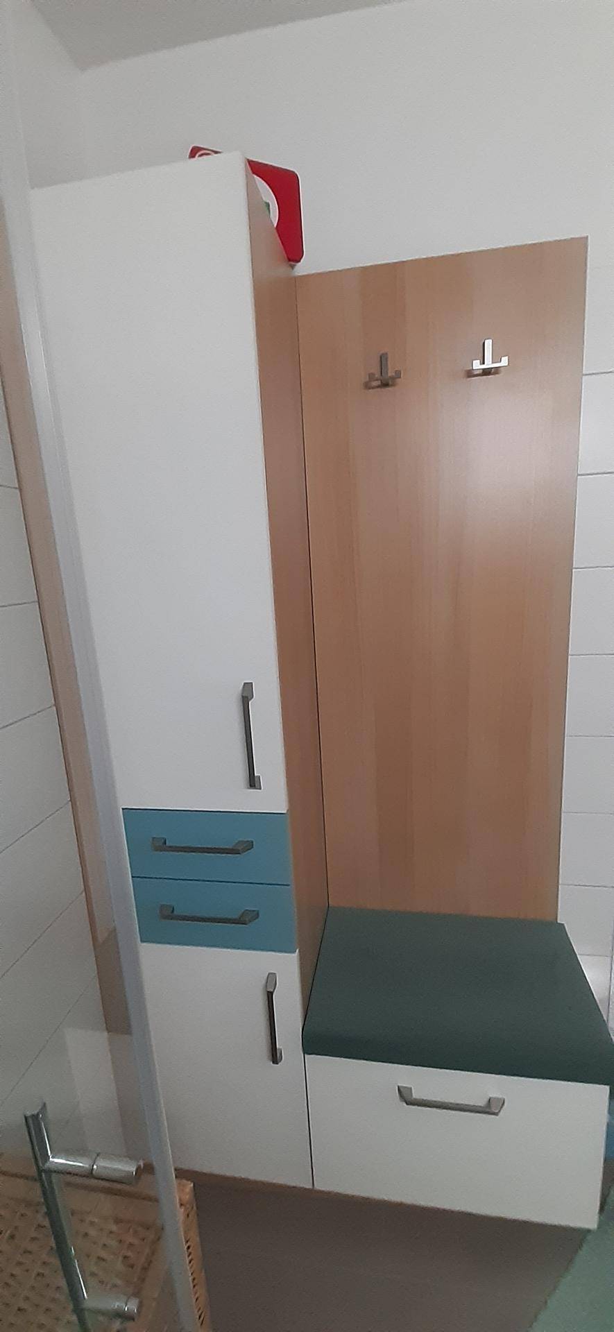 Moderner Flur mit hohem weißen Schrank, türkisfarbenen Schubladen und einer Garderobenwand in Holzoptik.