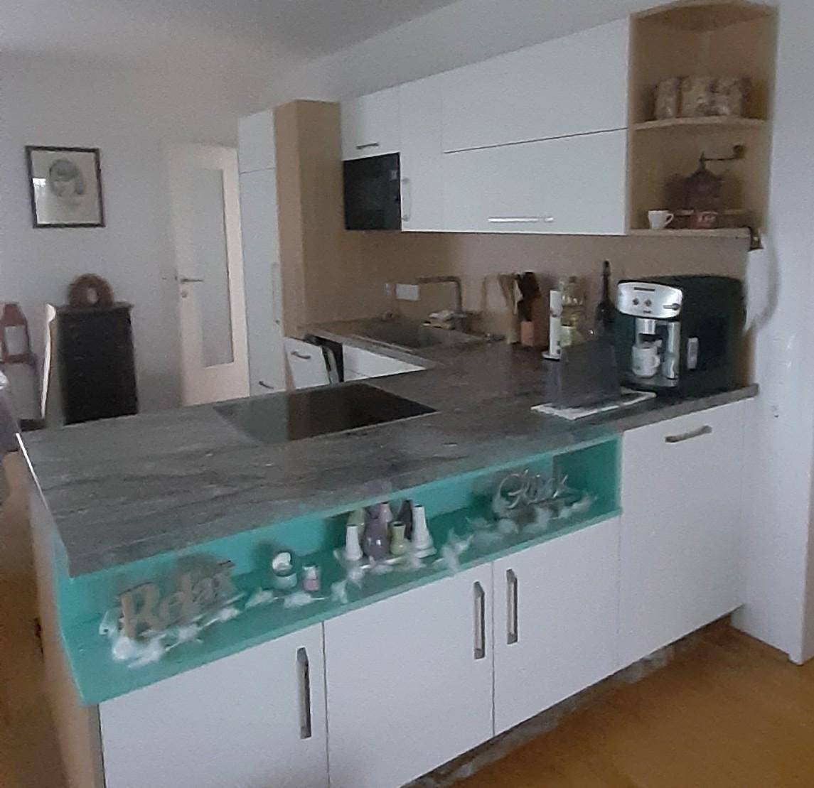 Moderne Küche mit weißen Schränken, grauer Arbeitsplatte und einer türkisfarbenen Theke mit integriertem Spülbecken.
