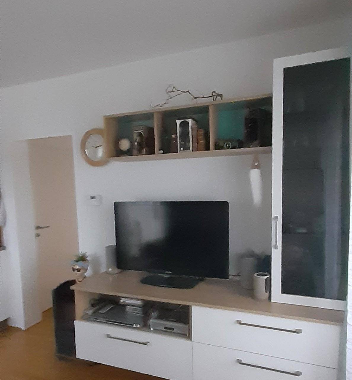 Wohnzimmerbereich mit modernem TV-Möbel, Wandregalen und einer weißen Tür, die den Raum hell erscheinen lässt.