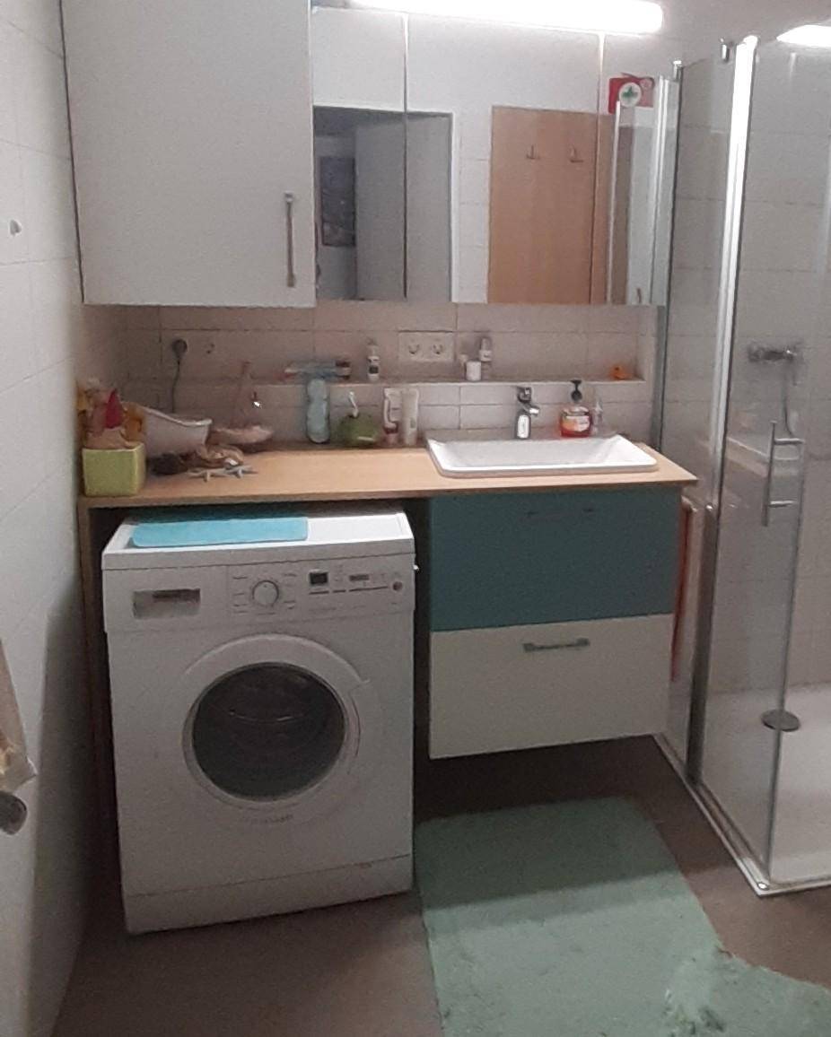 Badezimmer mit Waschbecken, Spiegelschrank, Duschkabine und einer integrierten Waschmaschine.