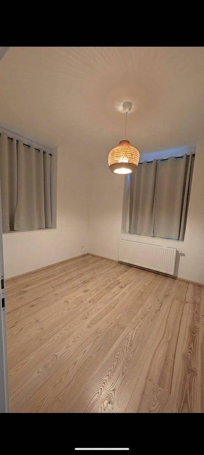 Geräumiges Schlafzimmer mit hellem Holzfußboden, zwei Fenstern und Deckenleuchte.