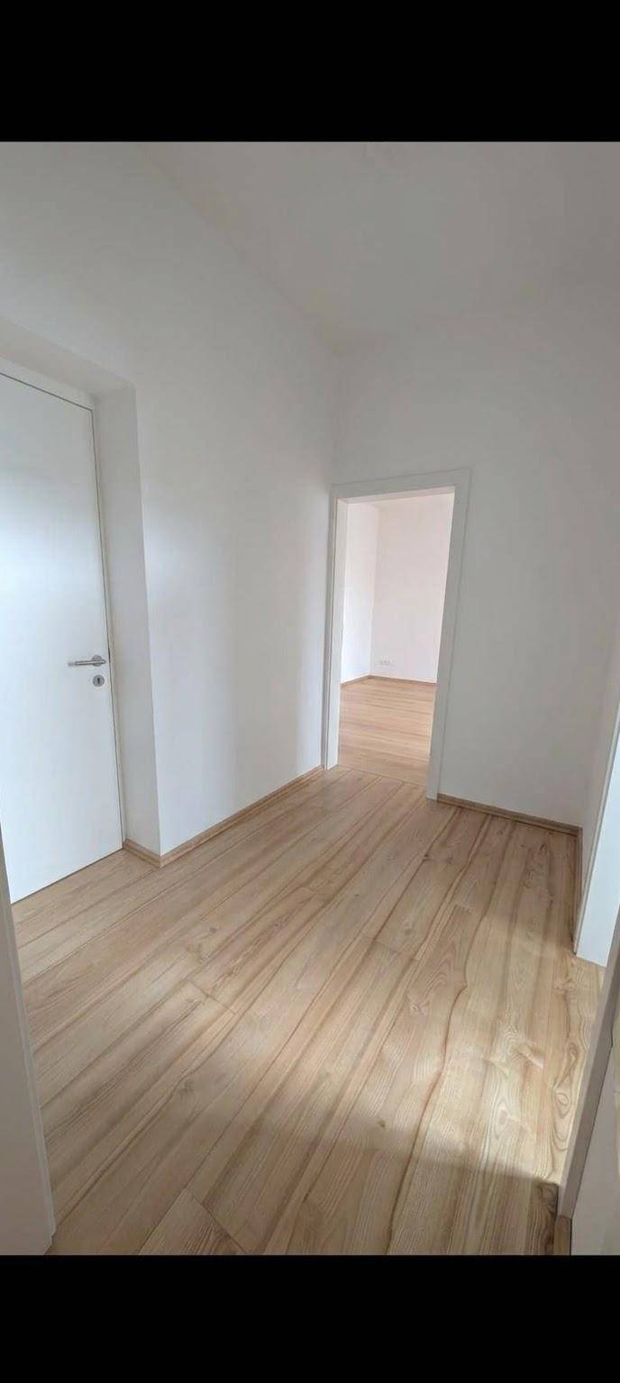 Heller Flur mit Holzfußboden und weißen Türen, der zu weiteren Räumen führt.