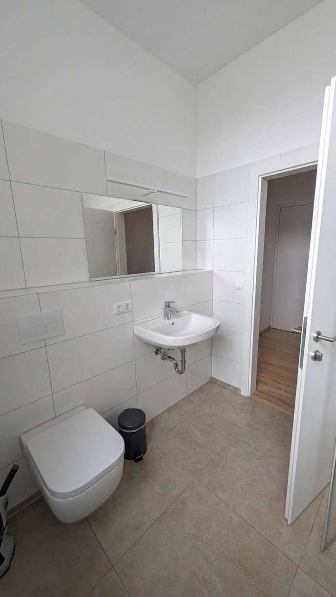Helles Badezimmer mit WC, Waschbecken, Spiegel und weißen Wandfliesen.