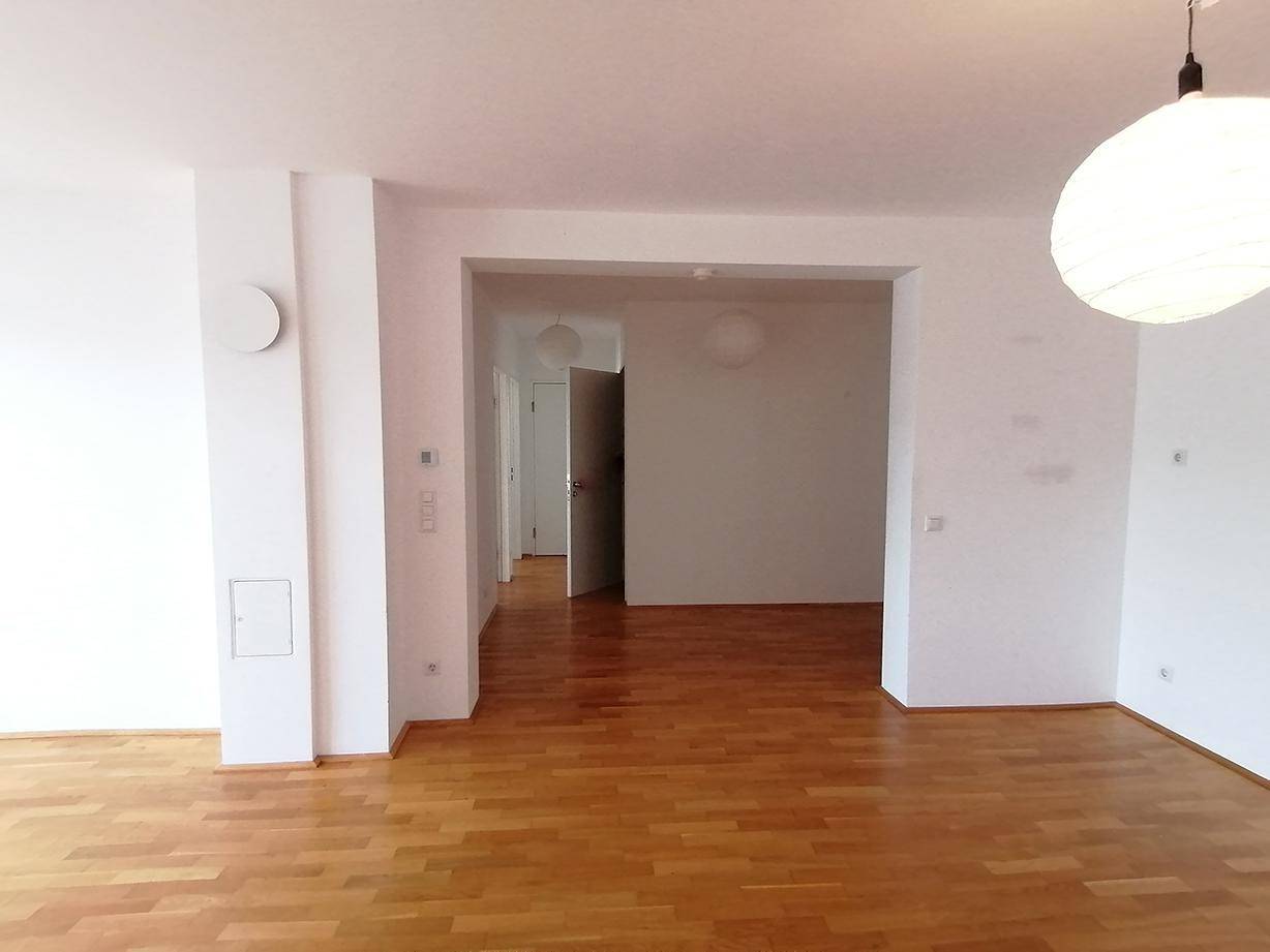Helles, leeres Wohnzimmer mit Parkettboden und Zugang zu weiteren Räumen.